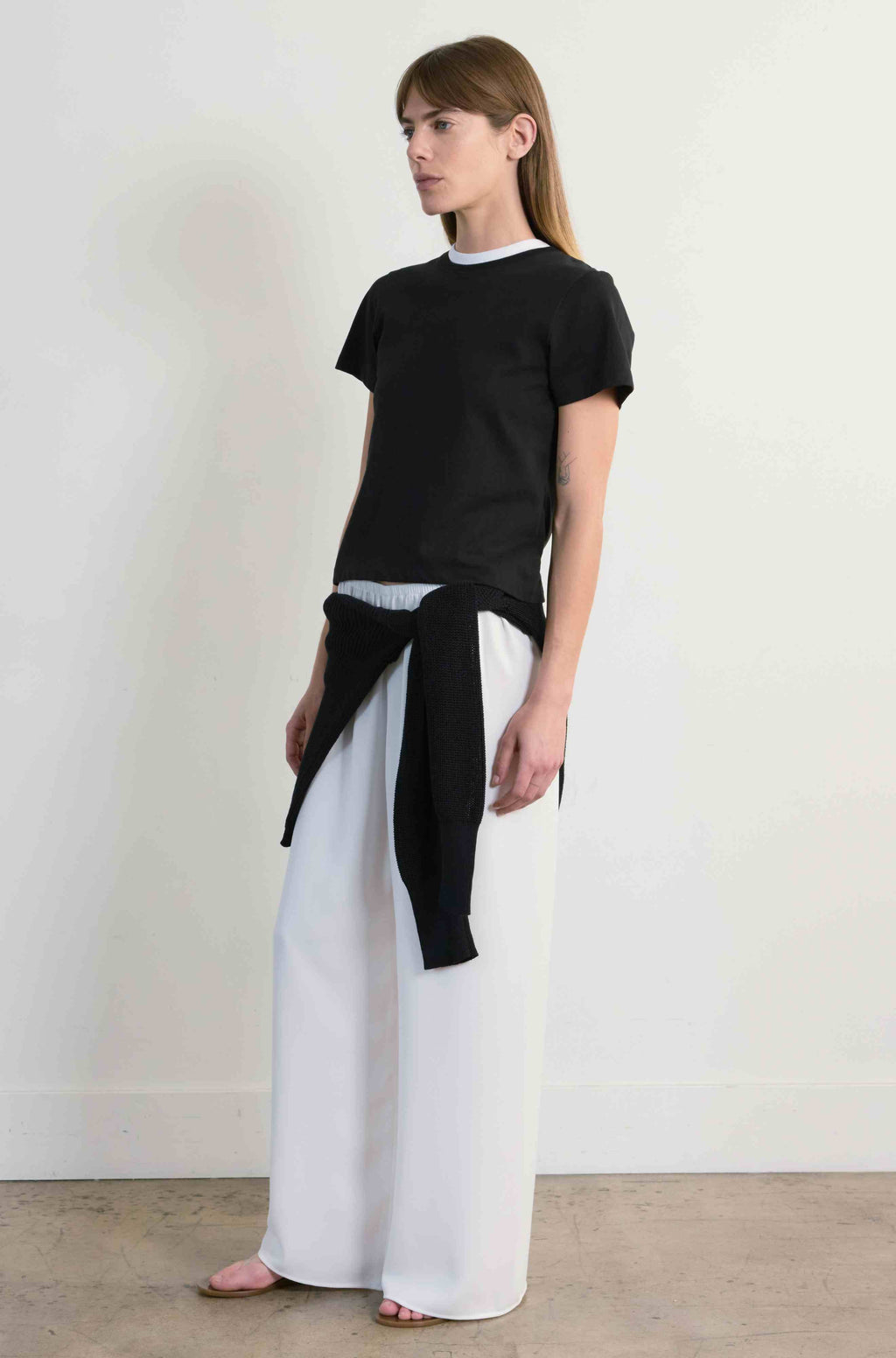 Woman wearing a black top and white pants against a plain background