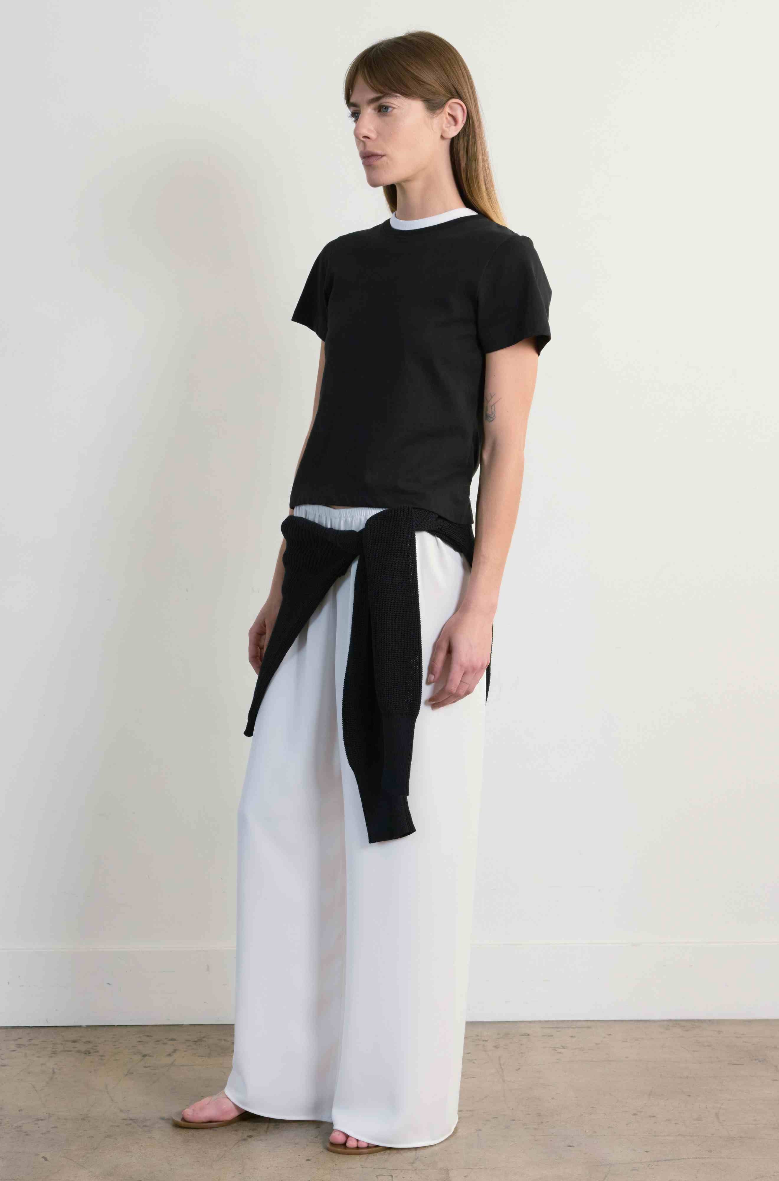 Woman wearing a black top and white pants against a plain background