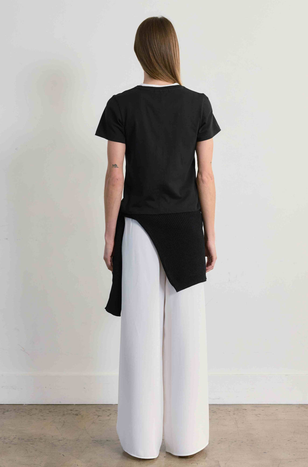 Person wearing a black top and white pants against a plain background