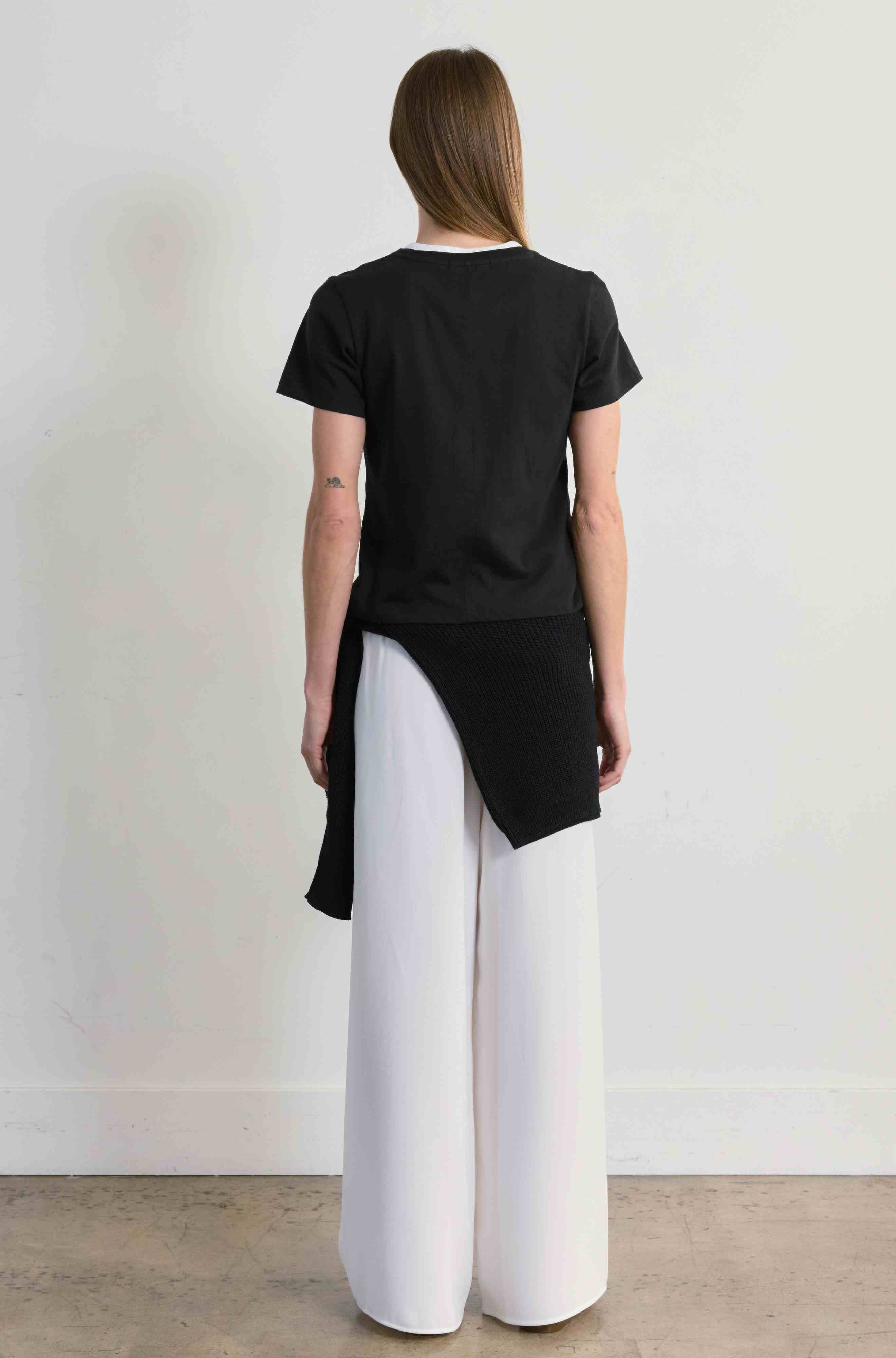 Person wearing a black top and white pants against a plain background