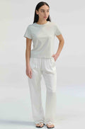 Woman wearing a light grey t-shirt with white pants on a light grey background
