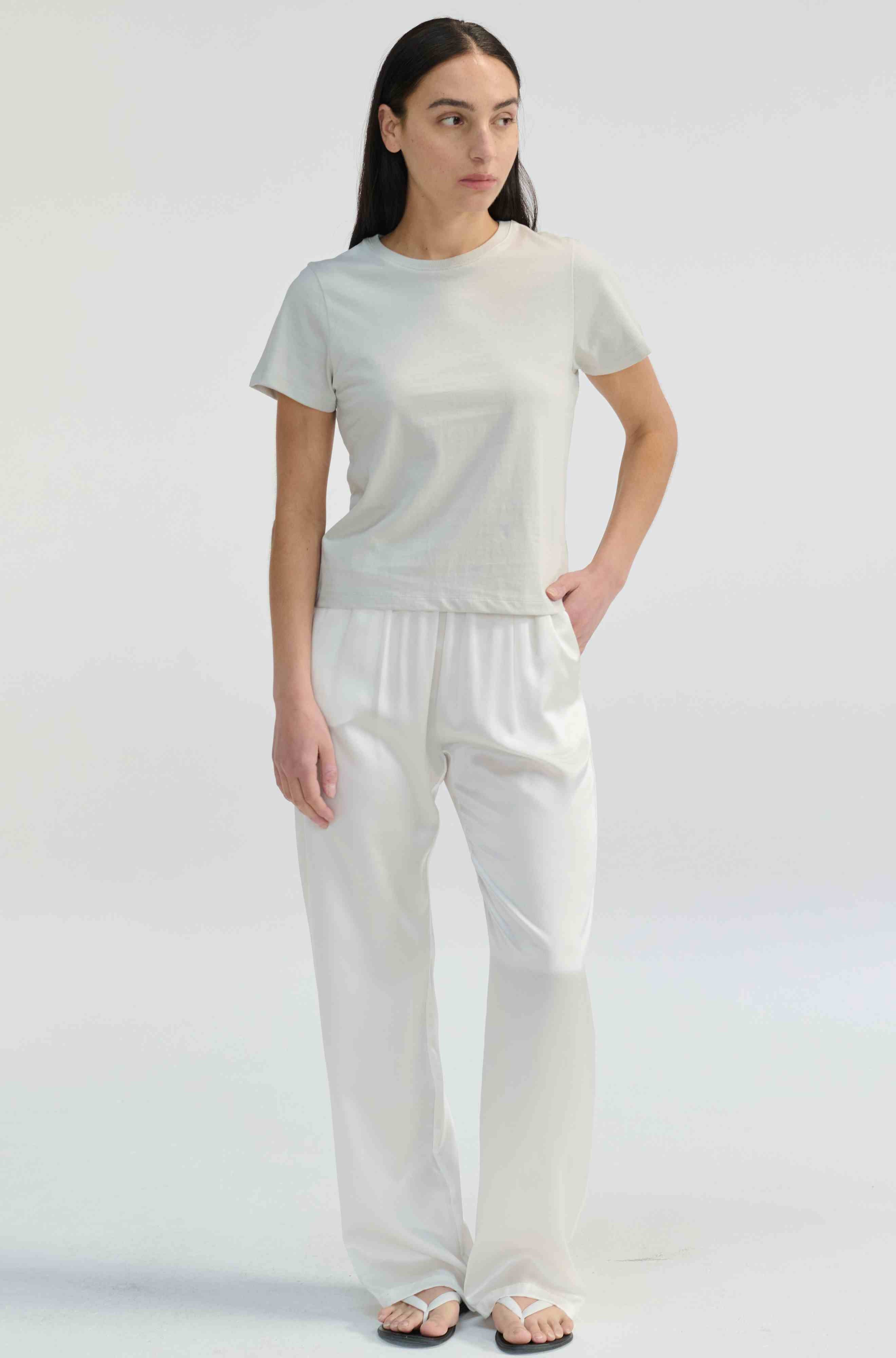 Woman wearing a light grey t-shirt with white pants on a light grey background