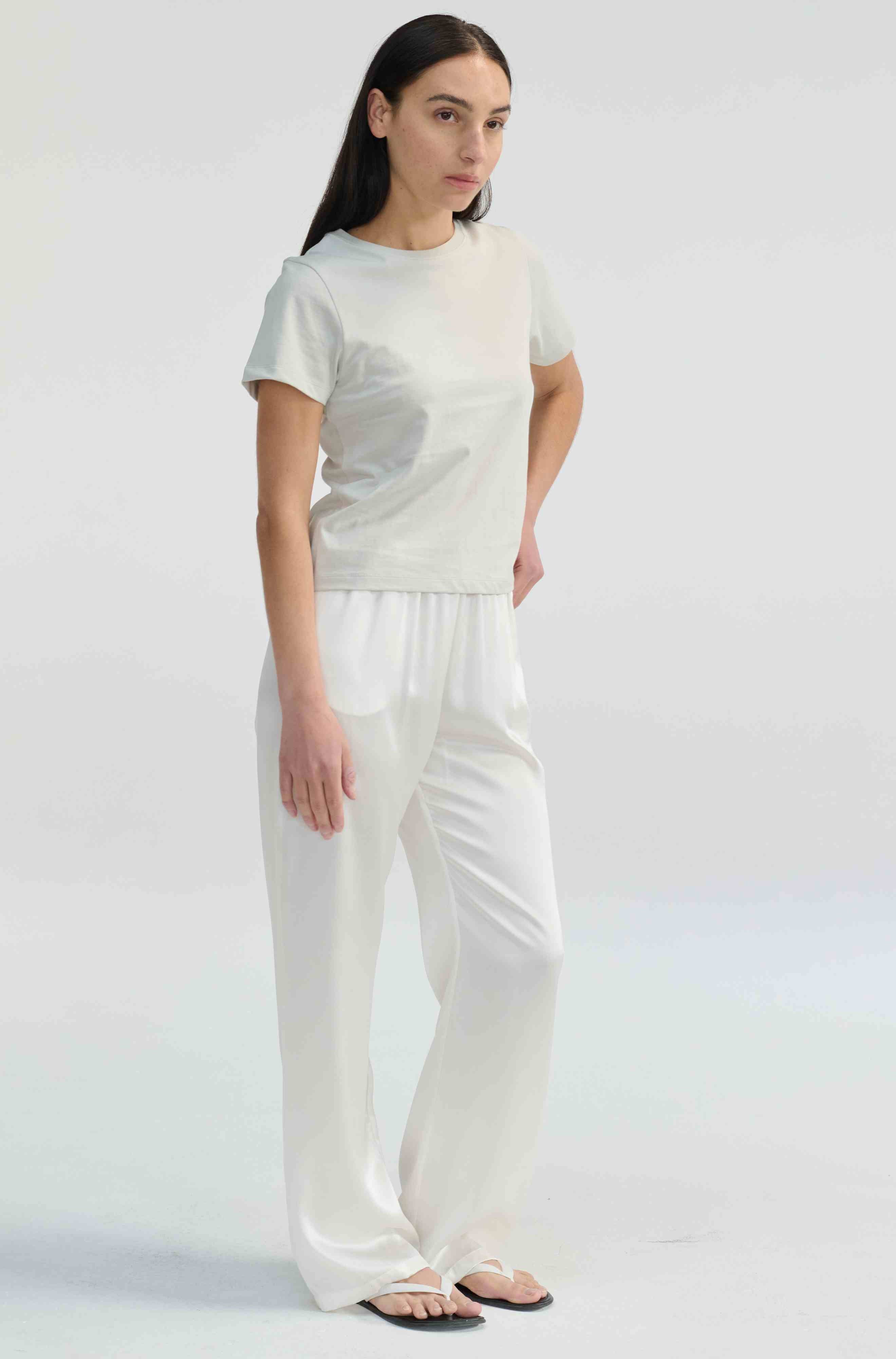 Woman wearing a light-colored top and white pants on a plain background