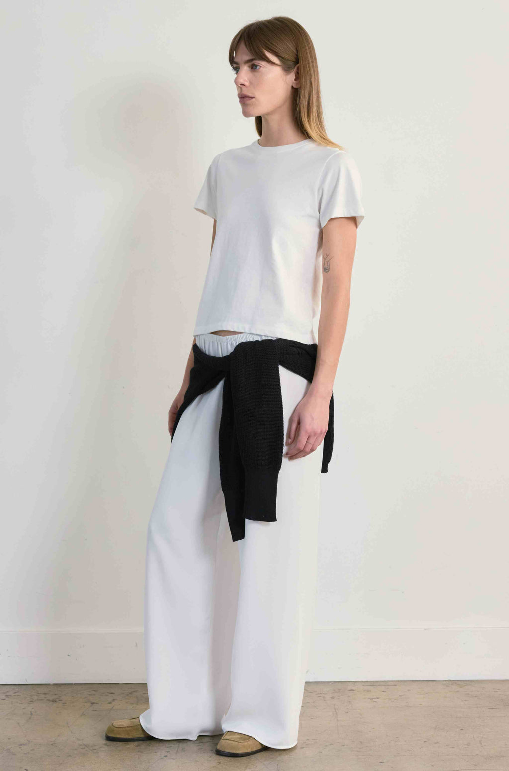 Woman wearing a white t-shirt and wide-leg pants with a black belt against a plain background