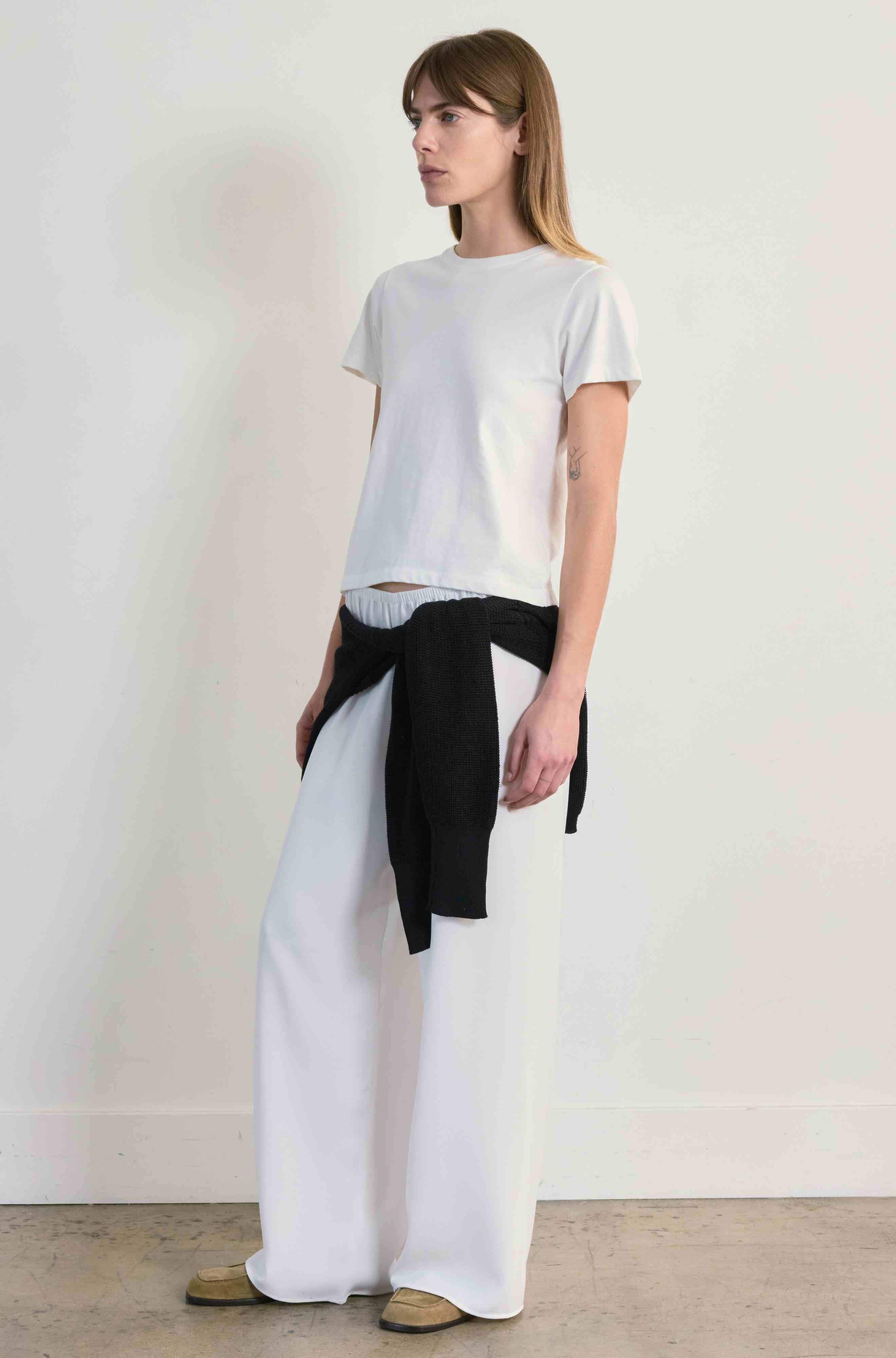 Woman wearing a white t-shirt and wide-leg pants with a black belt against a plain background