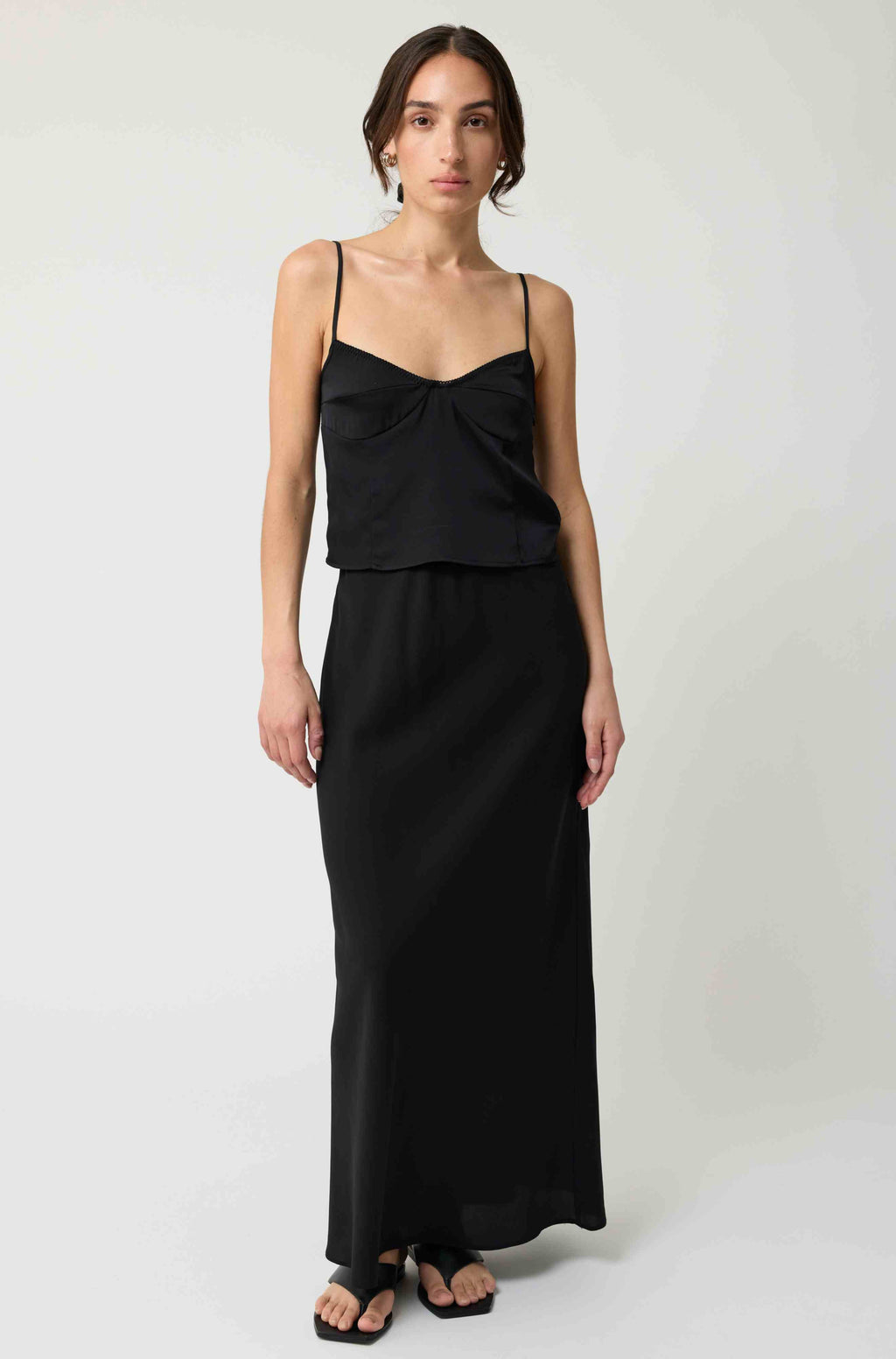 Woman wearing a black silk top and silk skirt against a white background