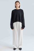 Person wearing a black sweater and white silk pants on a light gray background