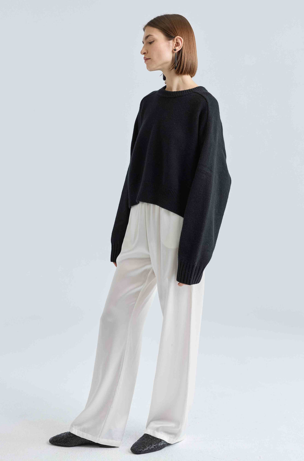 Person wearing a black sweater and white silk pants on a light gray background