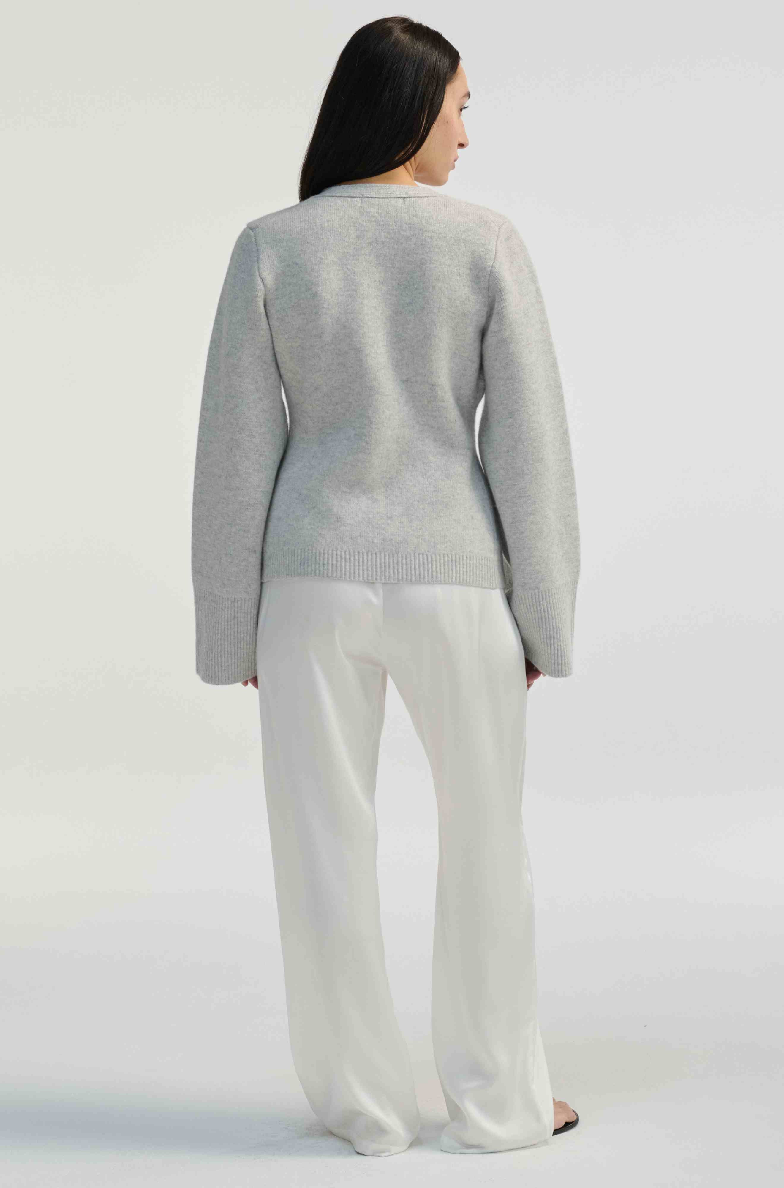 Person wearing a gray sweater and white silk pants on a white background