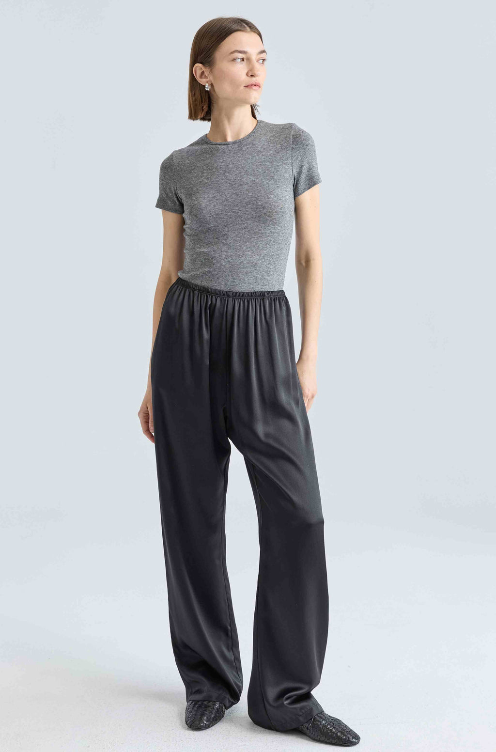 Woman wearing a gray top and black pants on a light gray background