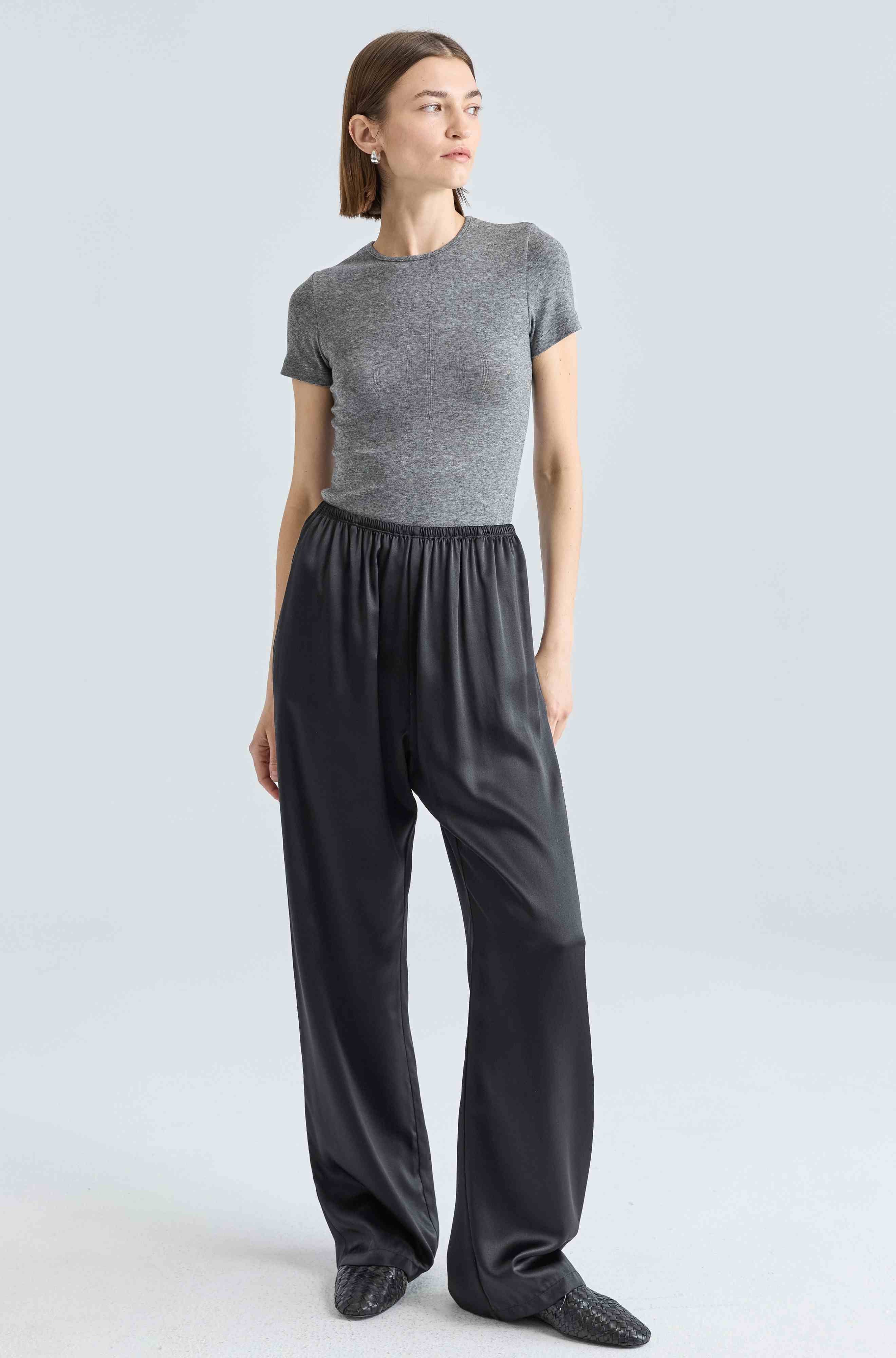 Woman wearing a gray top and black pants on a light gray background