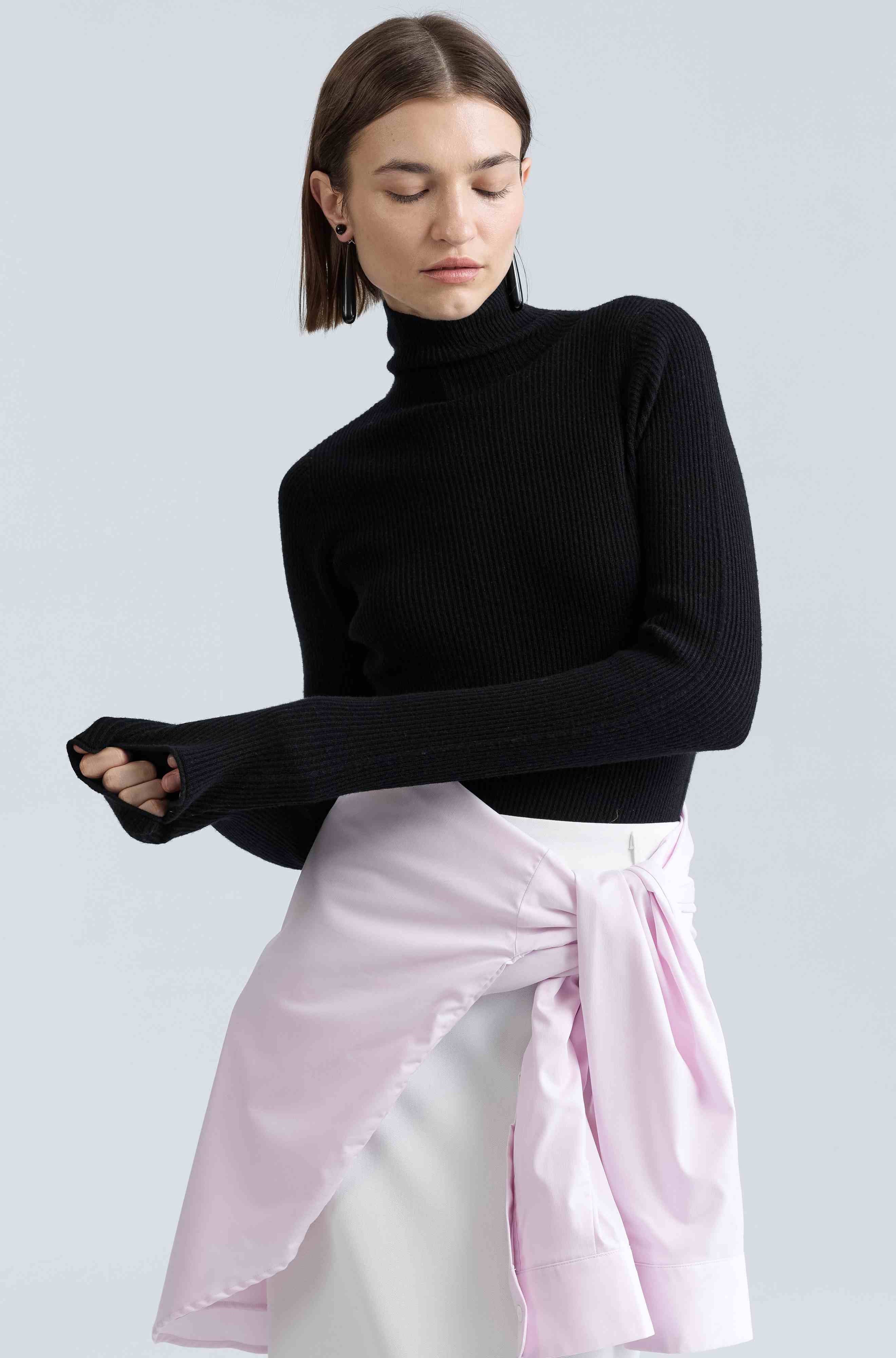 Woman wearing a black turtleneck and pink skirt against a light gray background