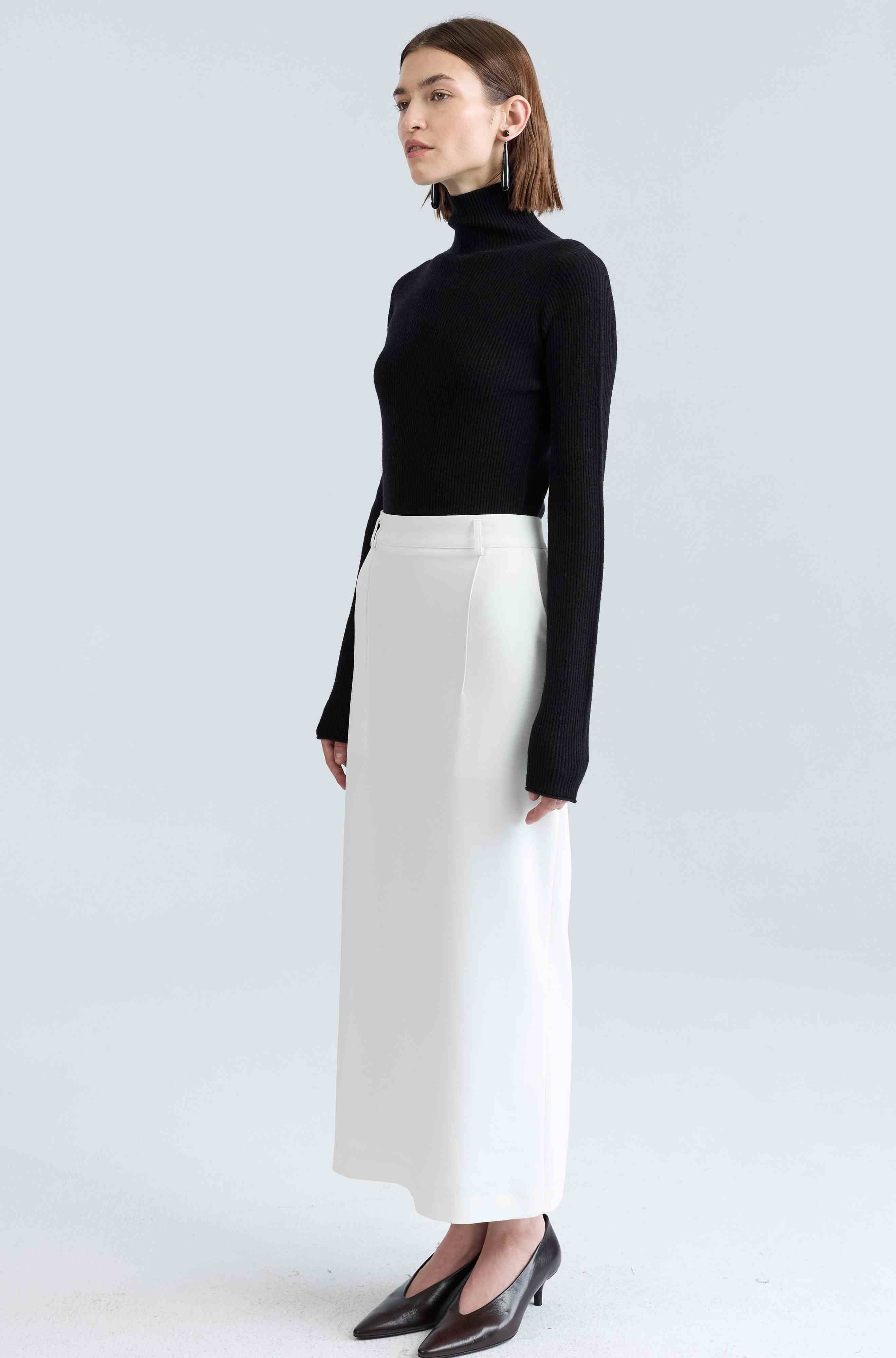 Woman wearing a black turtleneck and white skirt on a light gray background