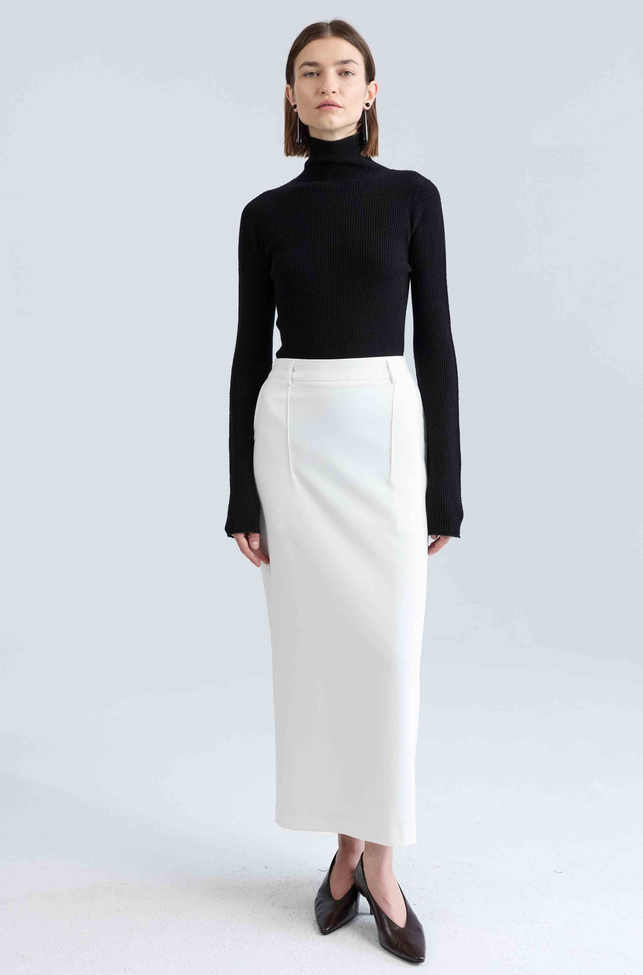 Person wearing a black turtleneck and white skirt on a light gray background