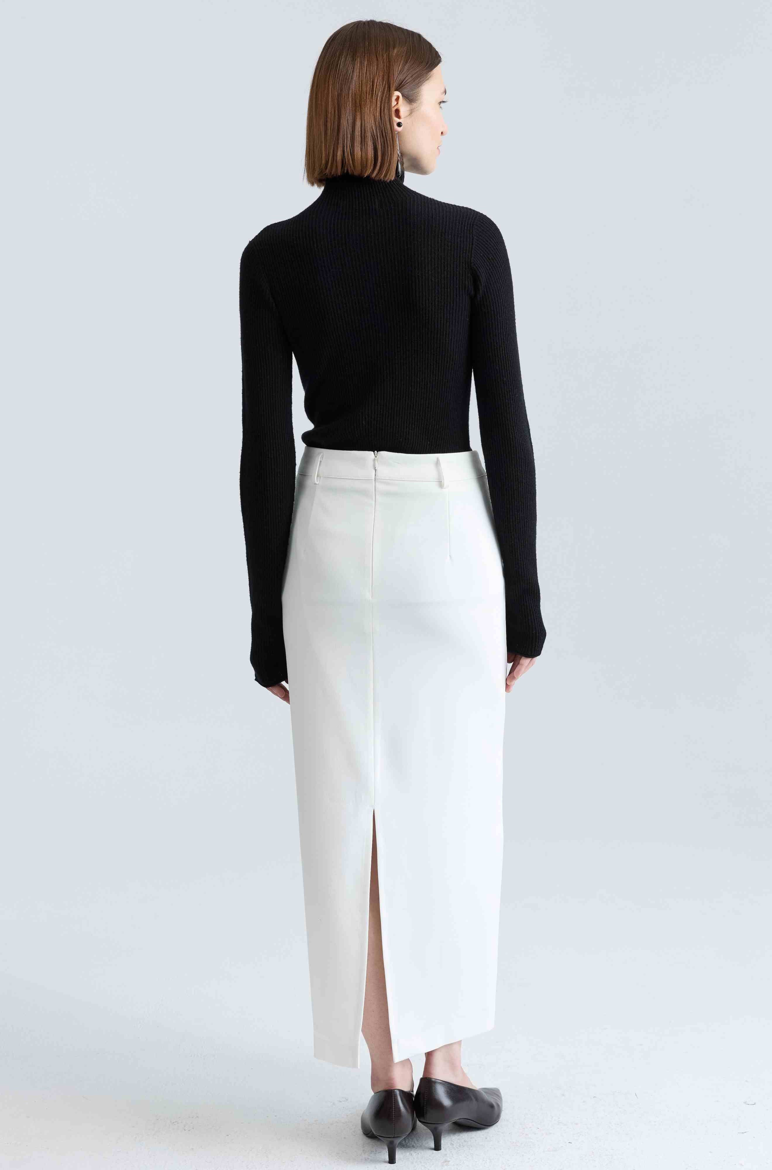 Woman wearing a black top and white skirt on a light gray background
