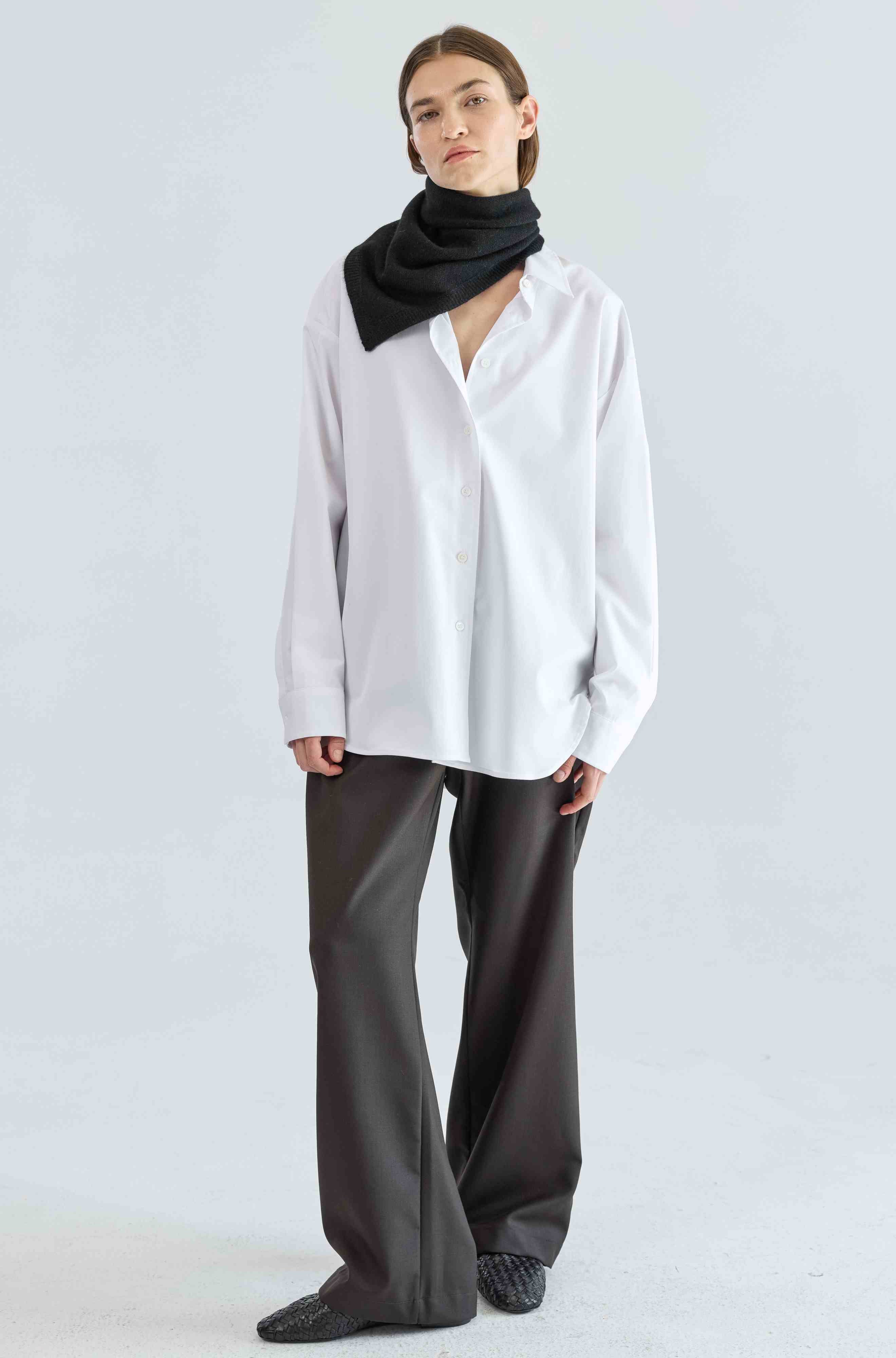Person wearing a white shirt, black scarf, and gray pants on a light gray background