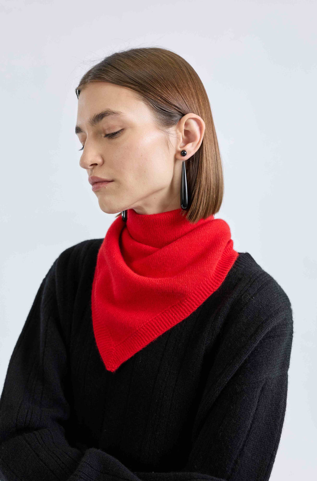 Woman wearing a red triangle scarf around her neck and a black sweater on a light grey background