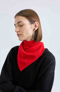 Woman wearing a red triangle scarf around her neck and a black sweater on a light grey background