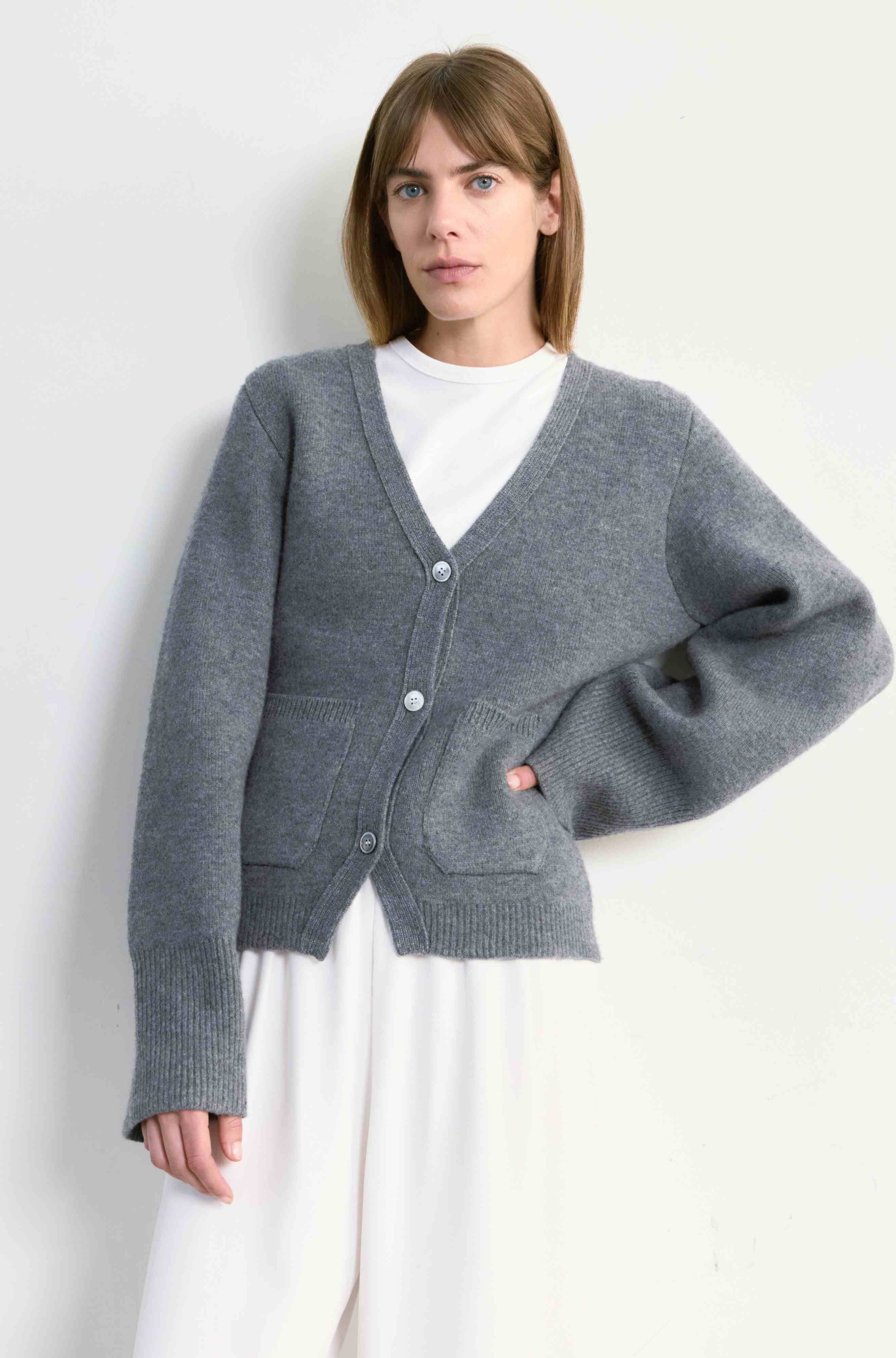 Woman wearing a gray cardigan over a white shirt against a plain background