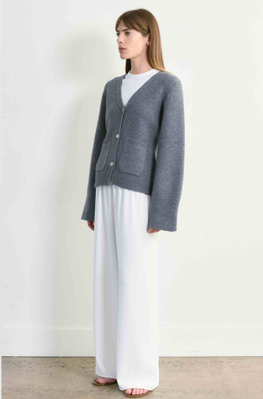 Woman wearing a gray cardigan over a white top and pants on a plain background