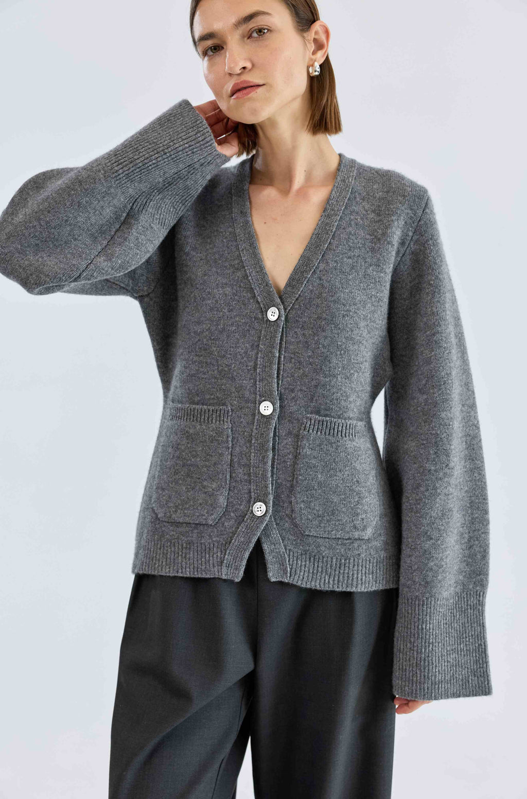 Person wearing a gray cardigan with a plain background