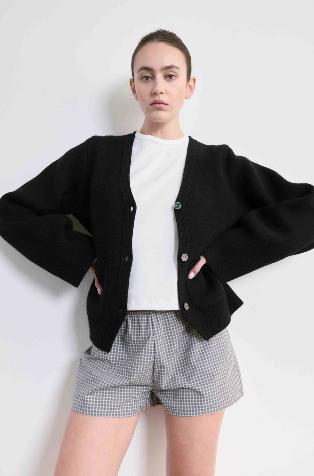 Person wearing a black cardigan, white shirt, and checkered shorts on a white background