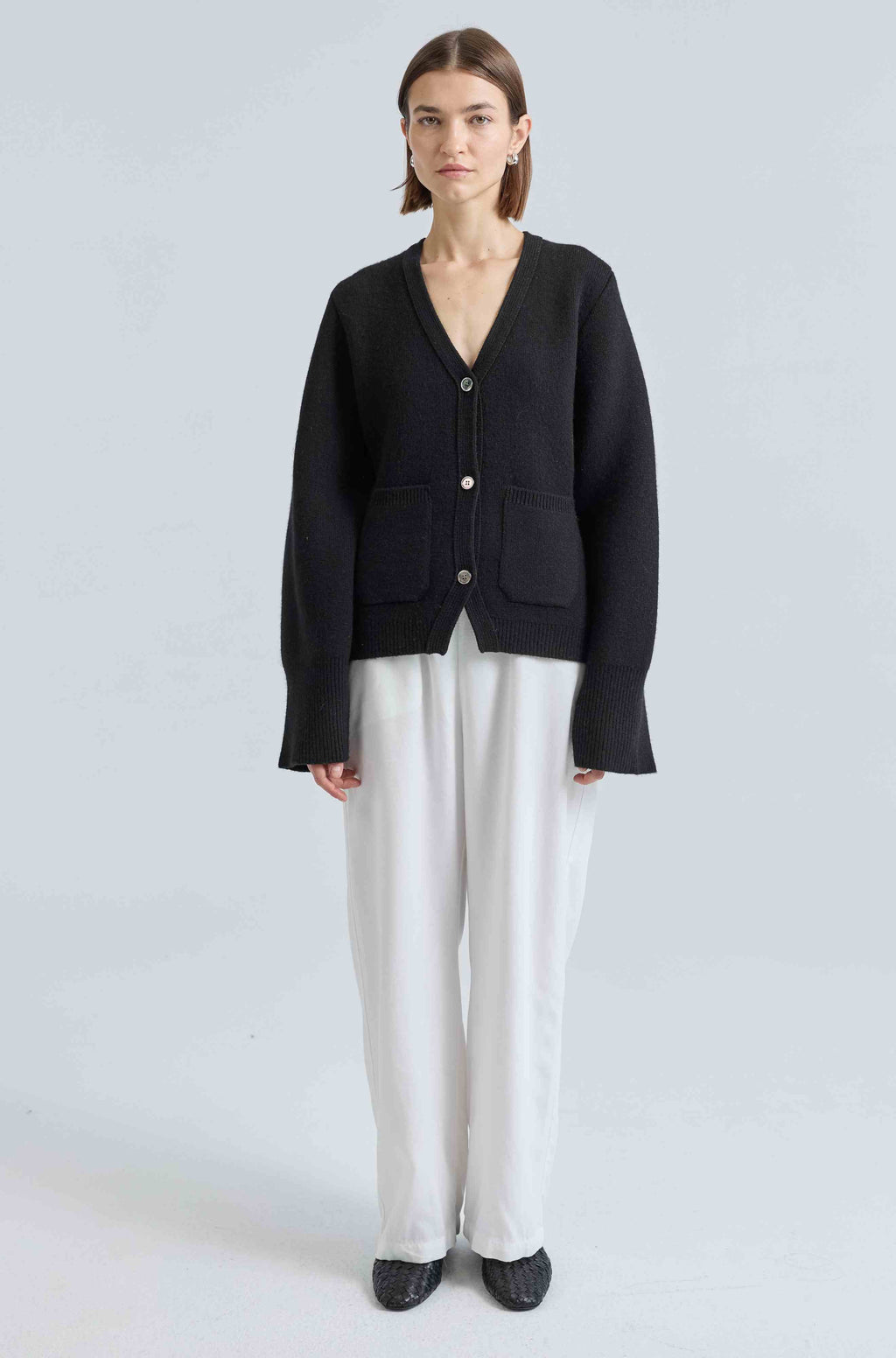 Person wearing a black cardigan and white pants on a light gray background