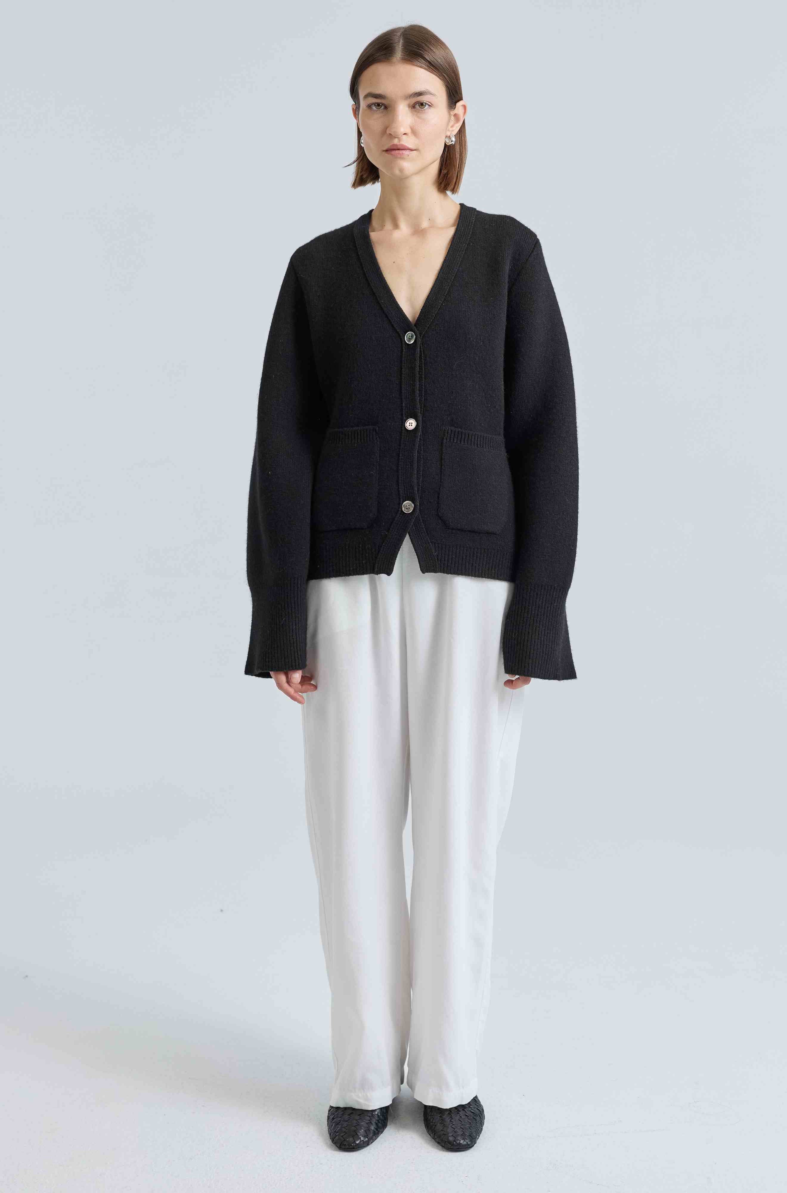 Person wearing a black cardigan and white pants on a light gray background