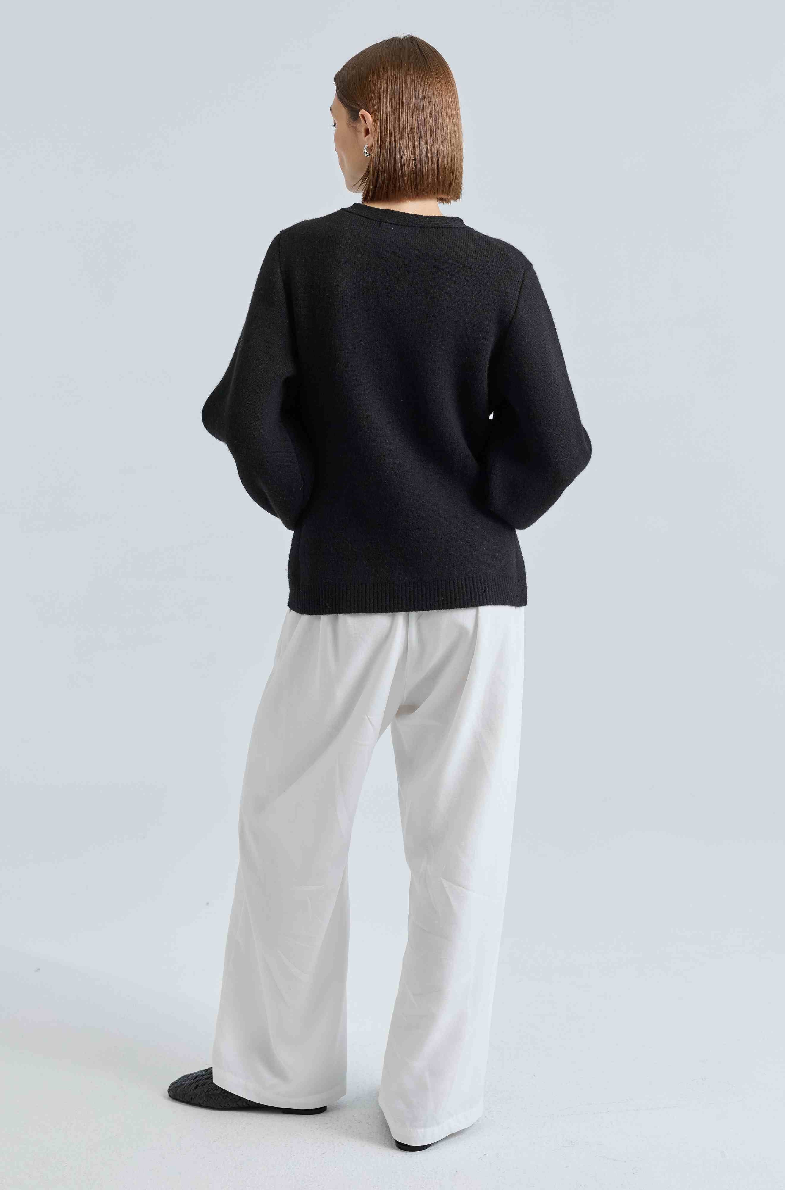 Person wearing a black sweater and white pants against a light gray background