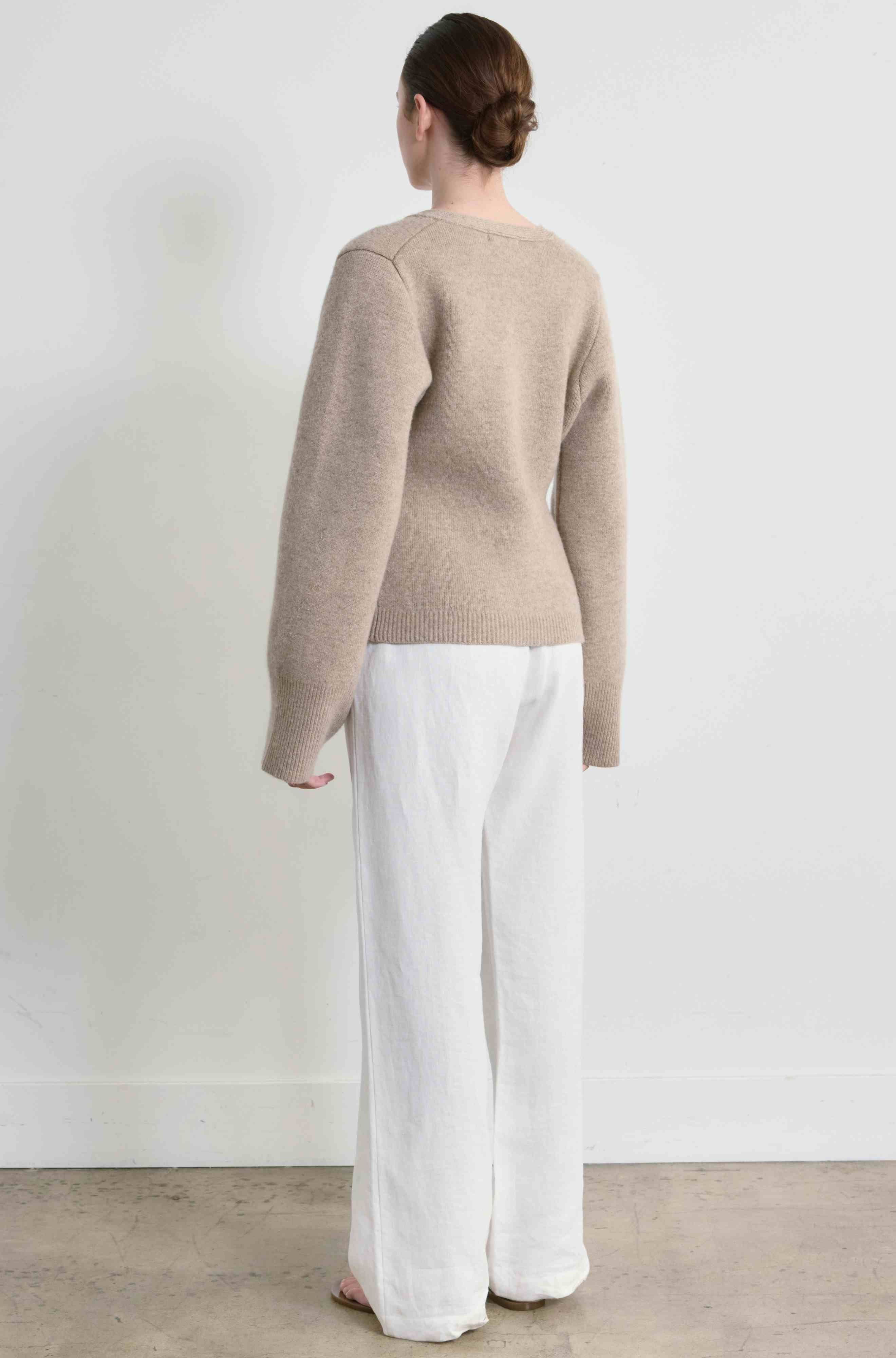 Person wearing a beige sweater and white pants against a plain background