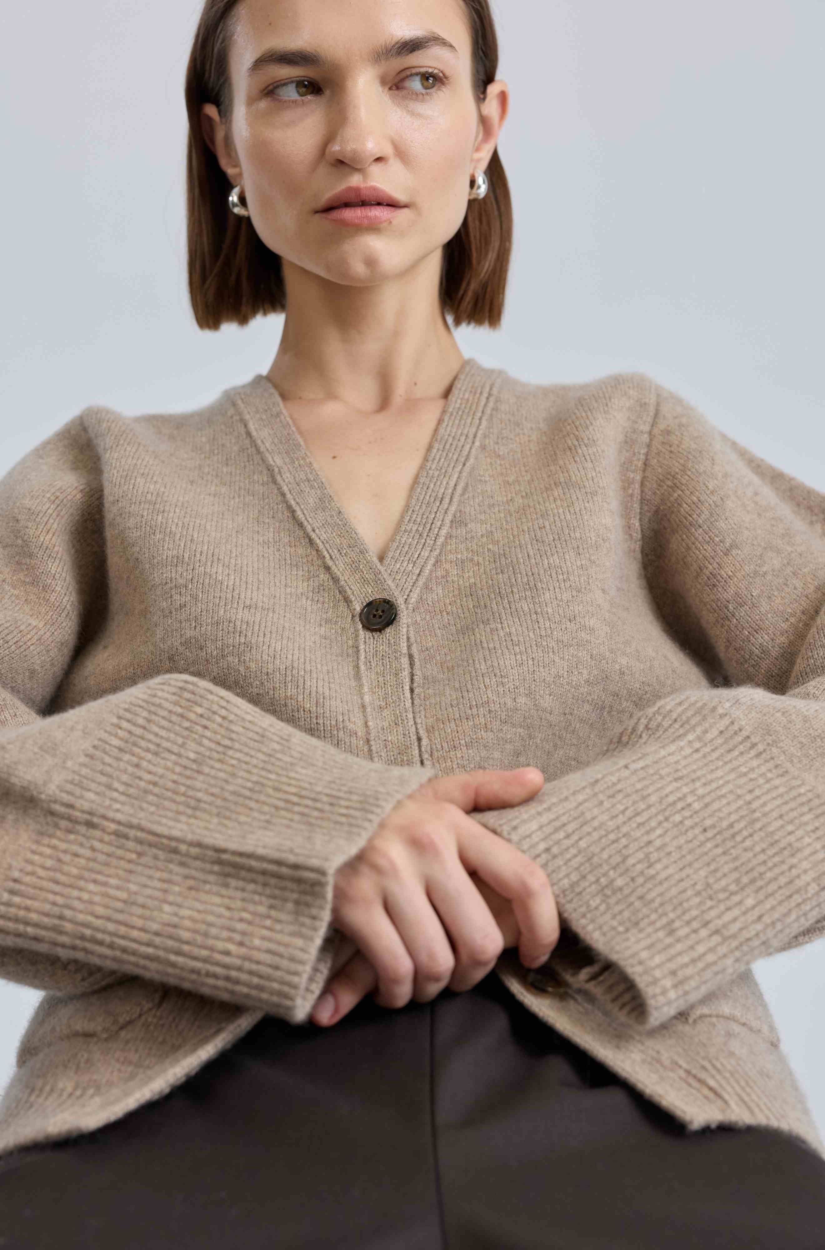 Woman wearing a beige cardigan against a light background
