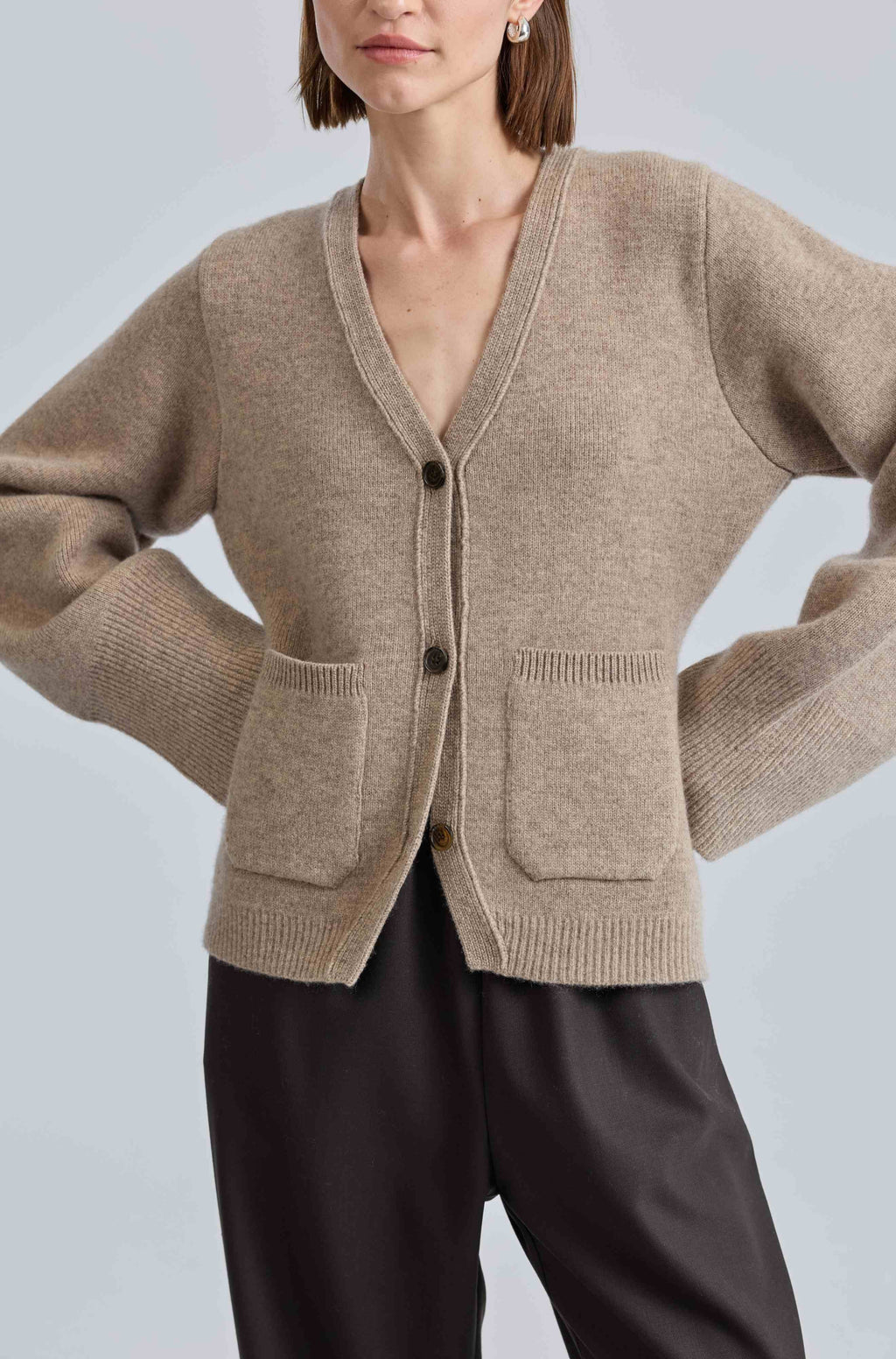 Person wearing a beige cardigan with black pants on a light gray background