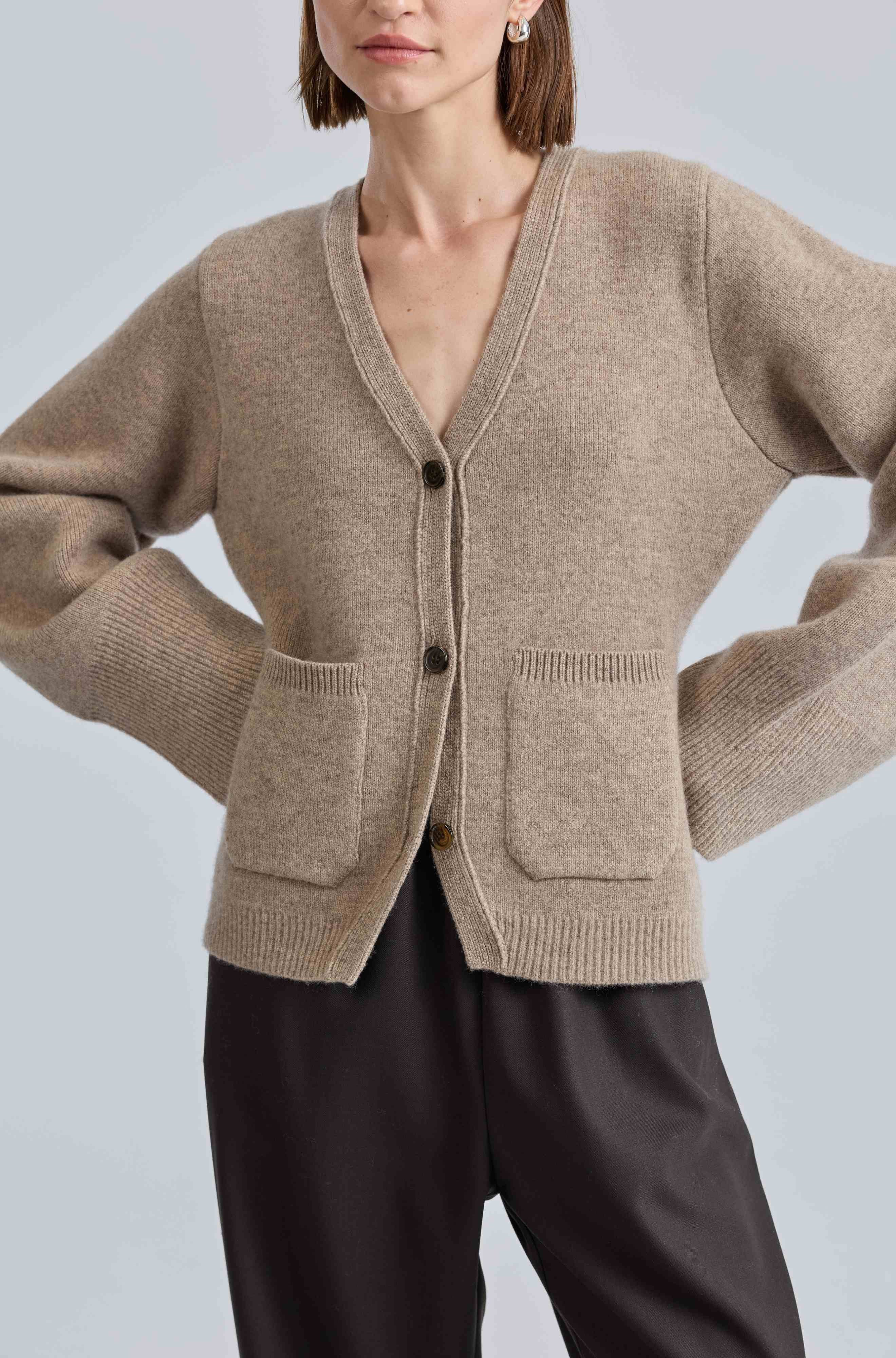 Person wearing a beige cardigan with black pants on a light gray background