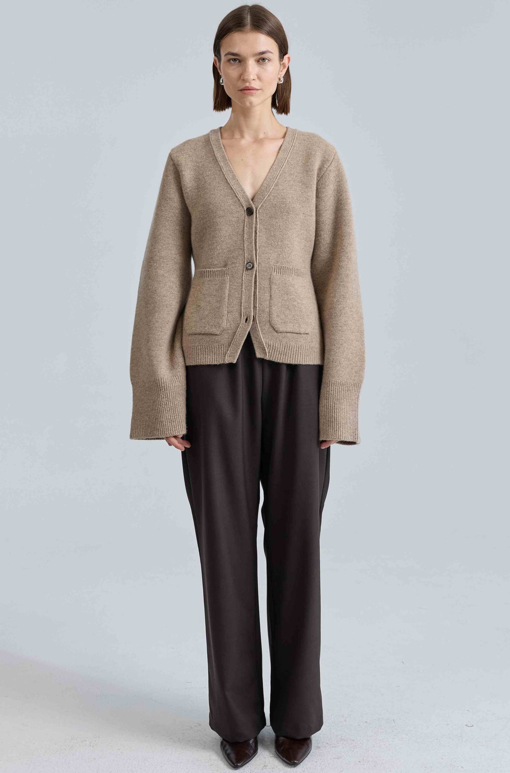 Woman wearing a beige cardigan and dark pants on a light gray background