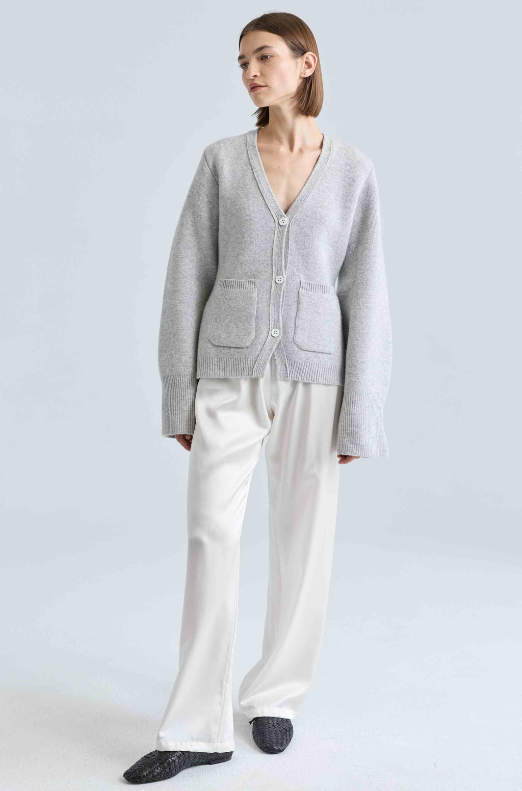 Person wearing a gray cardigan and white pants on a light gray background