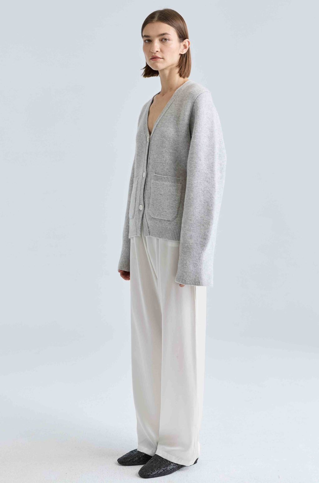 Person wearing a gray cardigan and white pants on a light gray background