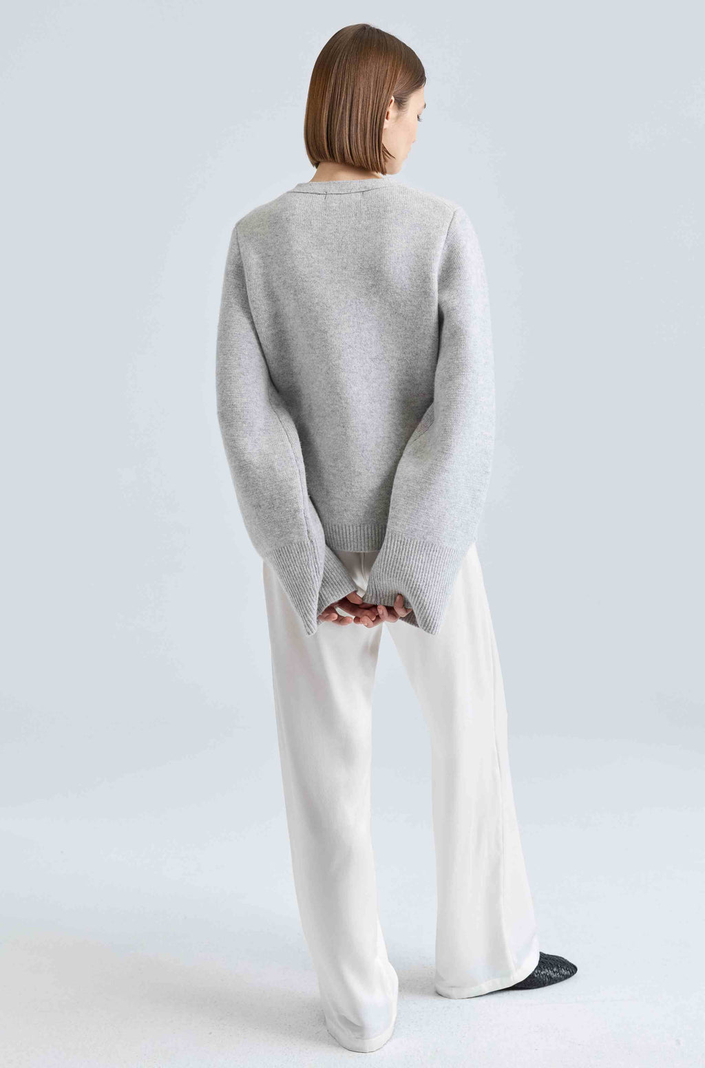 Person wearing a gray sweater and white pants on a light gray background
