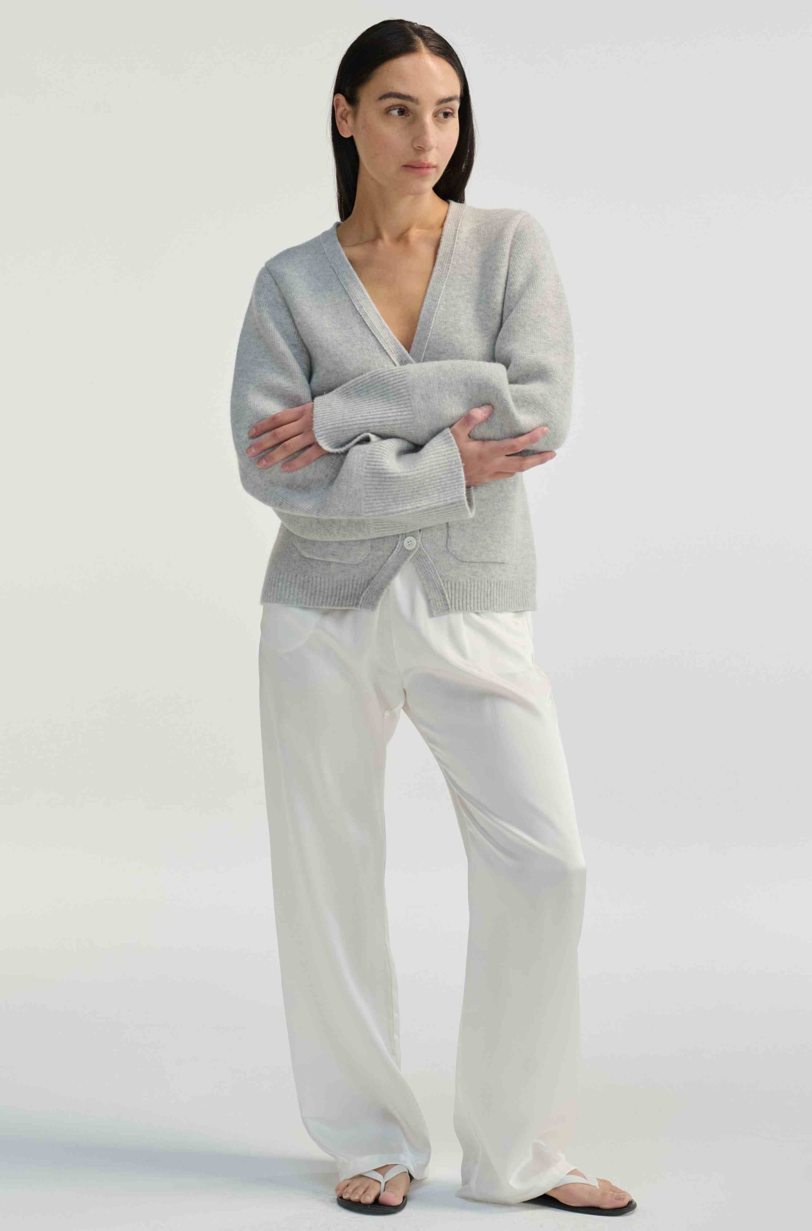 Woman wearing a gray sweater and white pants on a white background