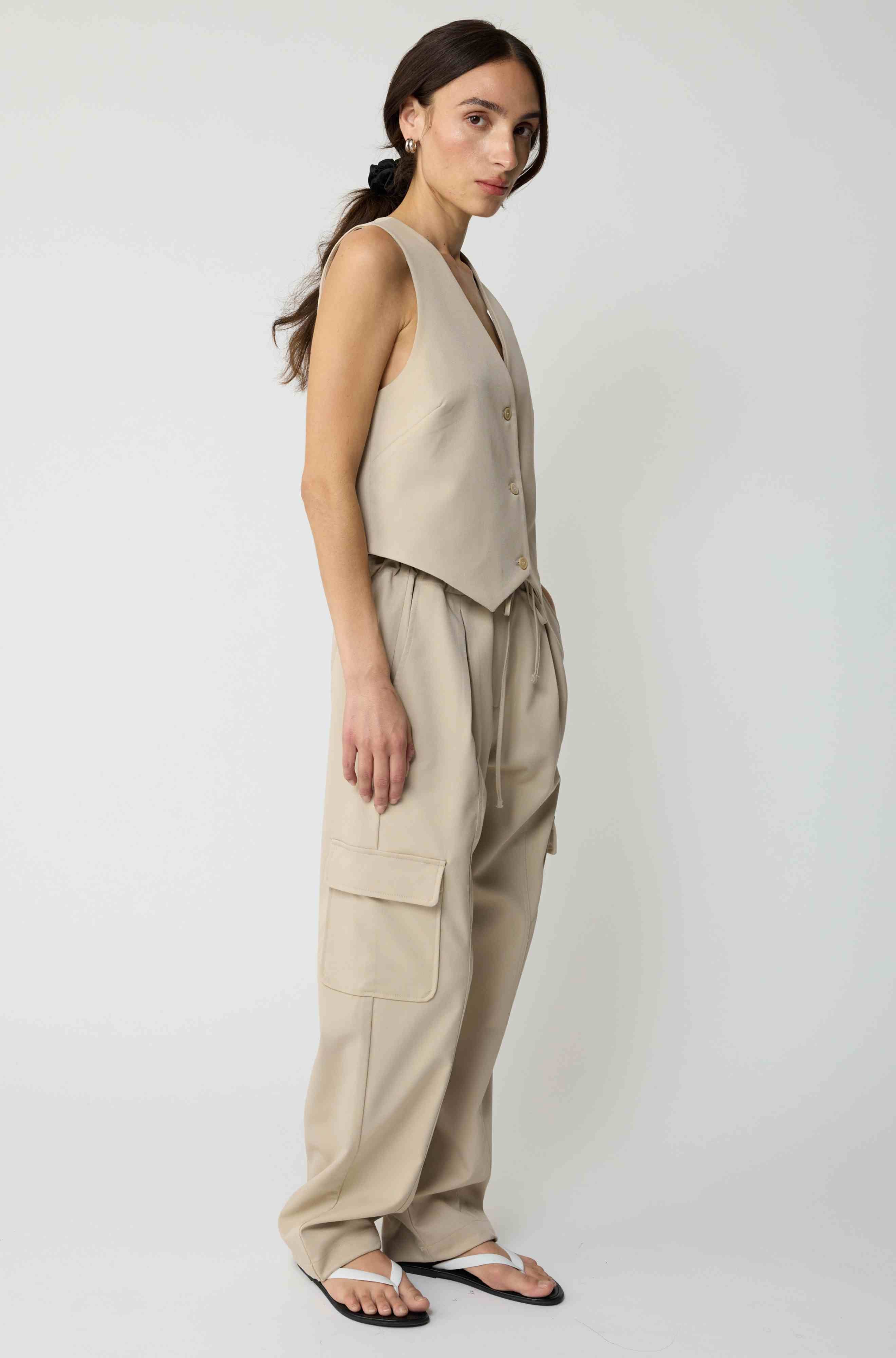 Woman wearing a beige tencel button up vest with beige cargo pants on a light grey background
