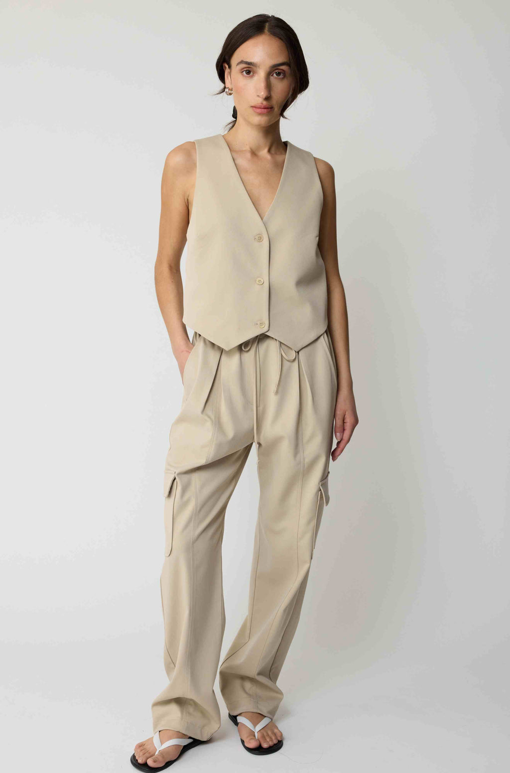 Woman wearing a beige tencel button up vest with beige cargo pants on a light grey background