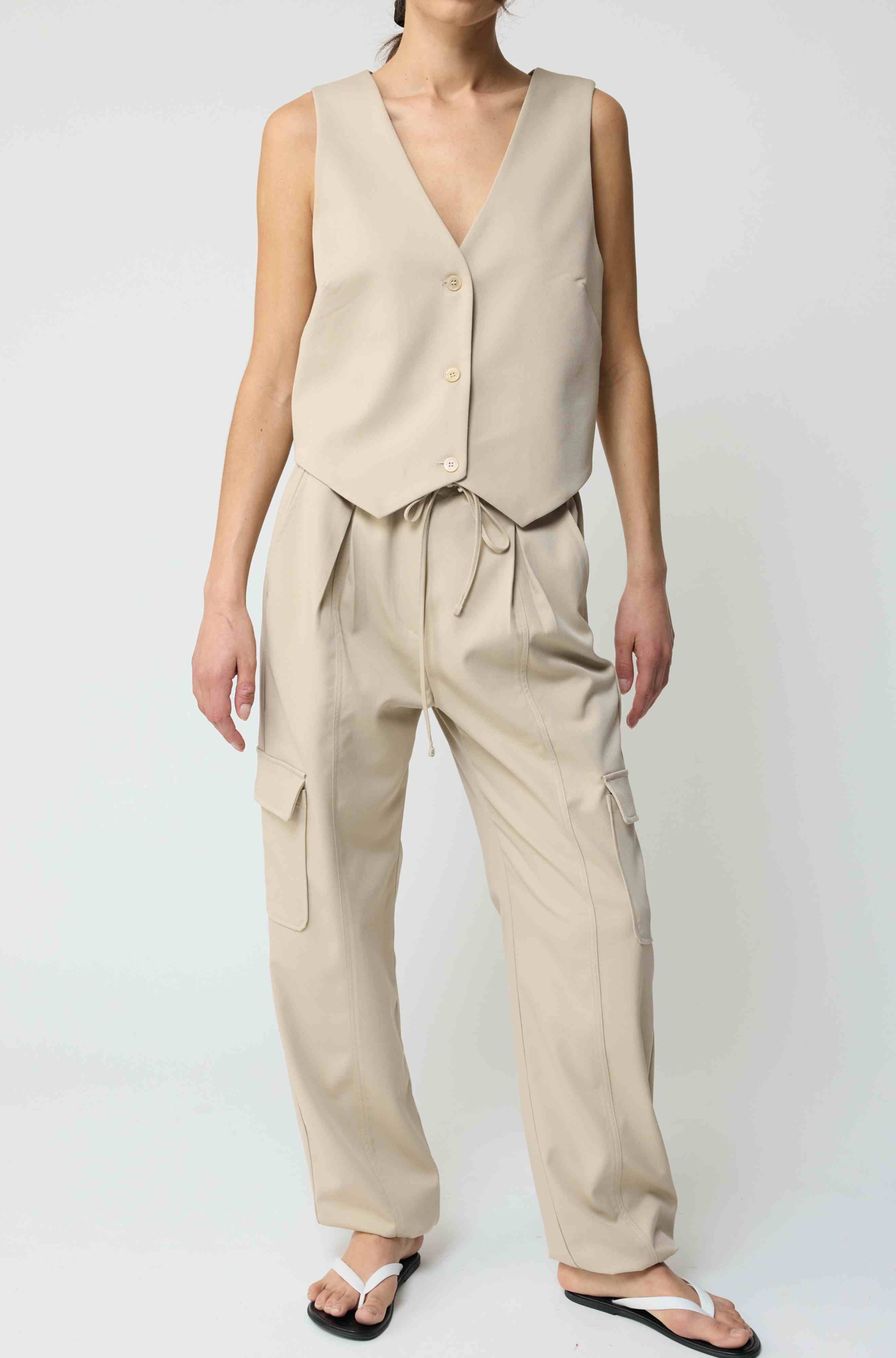 Woman wearing a beige tencel button up vest with beige cargo pants on a light grey background