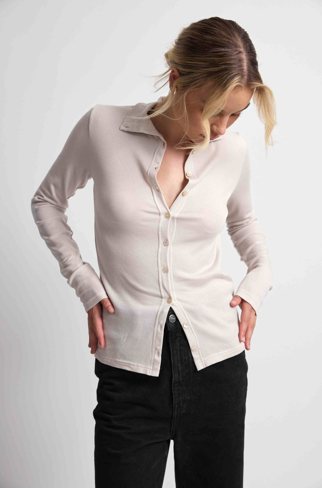 Woman wearing a pink button up top with black bottoms on a light grey background