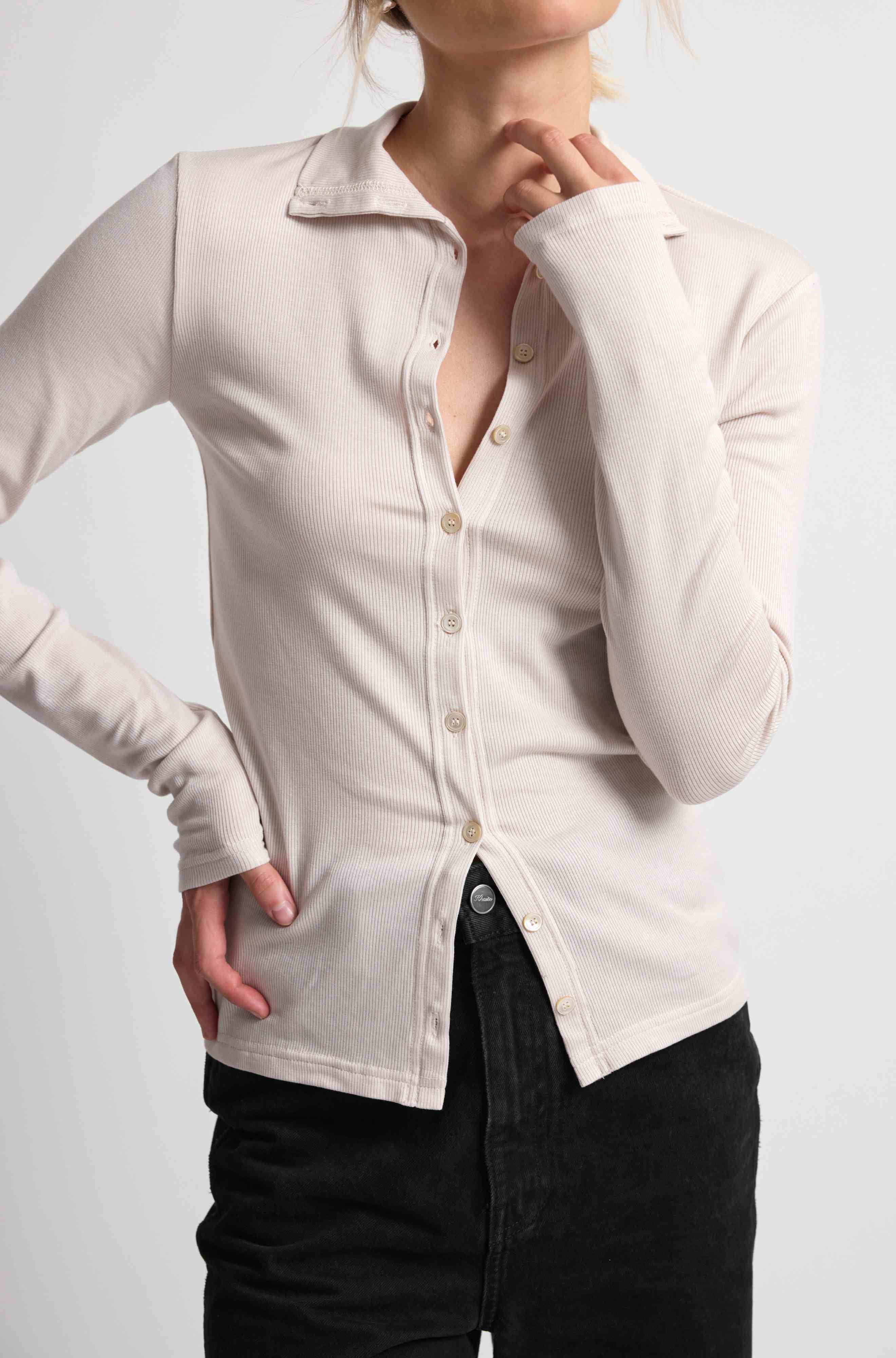 Woman wearing a pink button up top with black bottoms on a light grey background