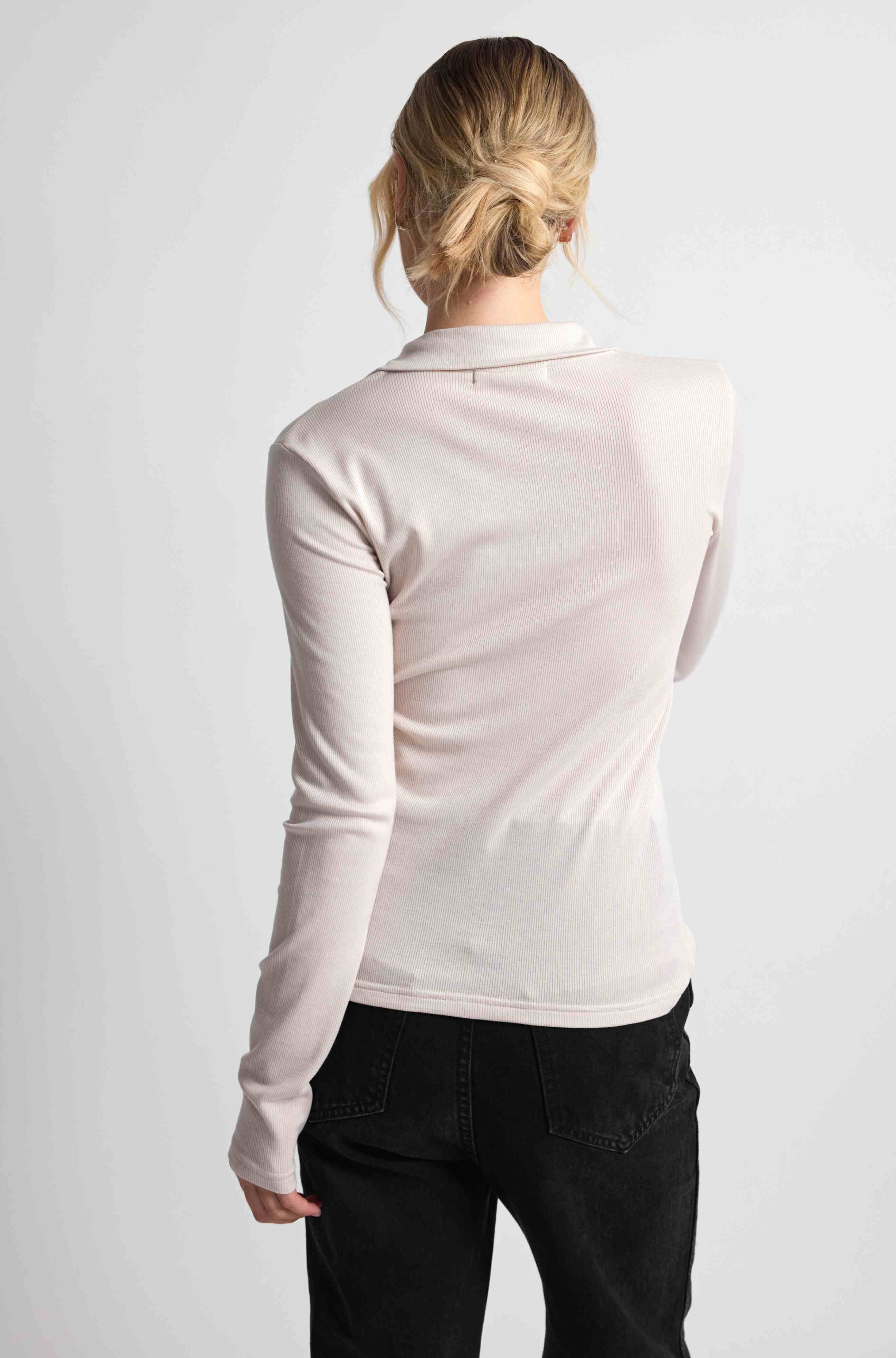 Woman wearing a pink button up top with black bottoms on a light grey background