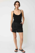 Woman wearing a black tank top and black linen shorts against a light grey background