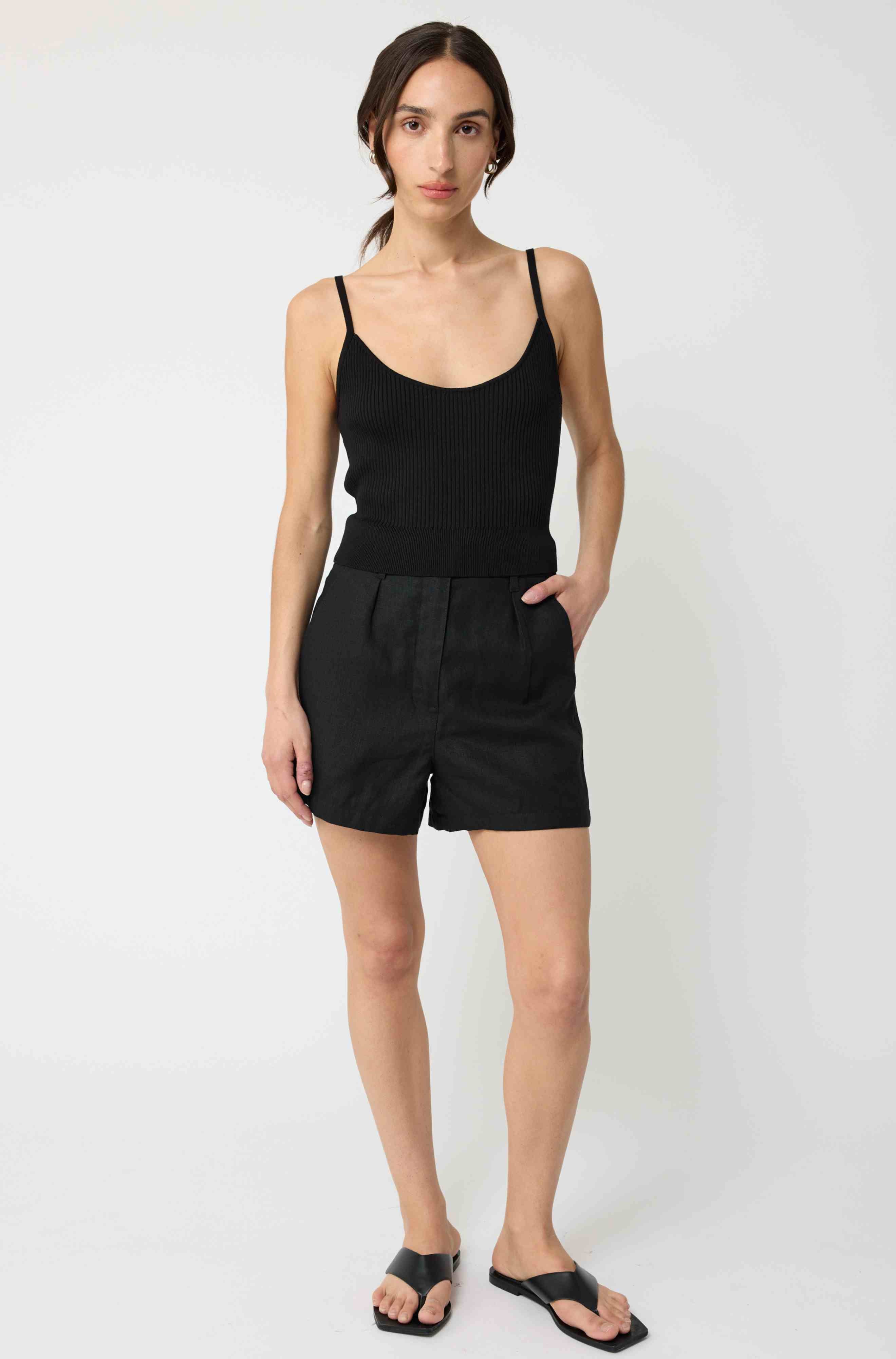 Woman wearing a black tank top and black linen shorts against a light grey background