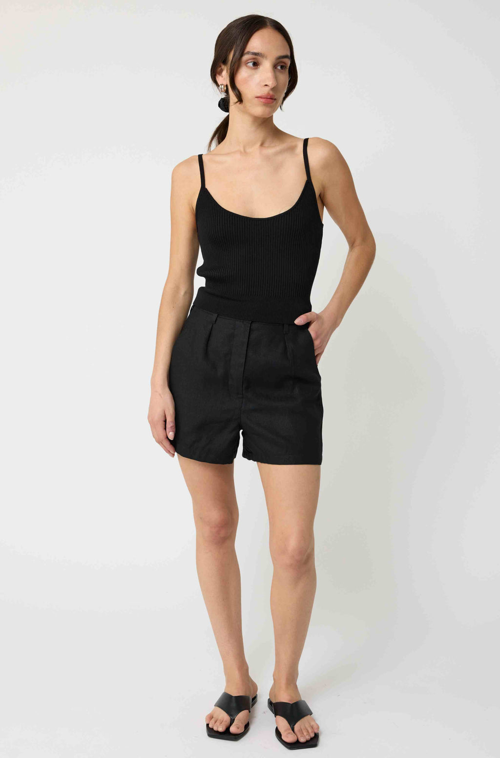 Woman wearing a black tank top and black linen shorts against a light grey background
