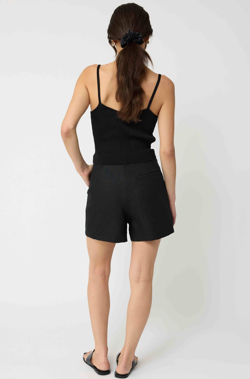 Woman wearing a black tank top and black linen shorts against a light grey background
