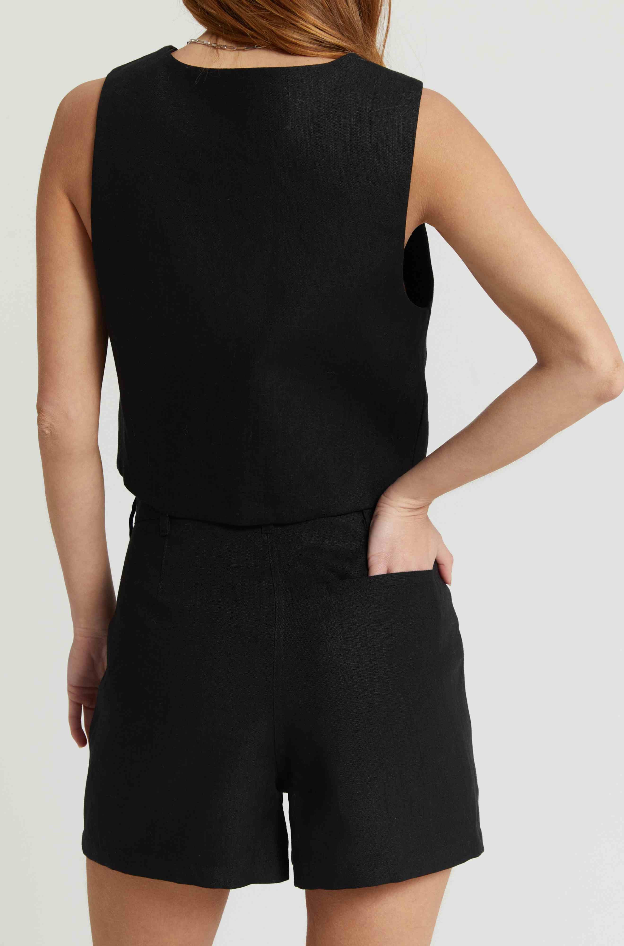 Woman wearing a black vest and black linen shorts against a light grey background