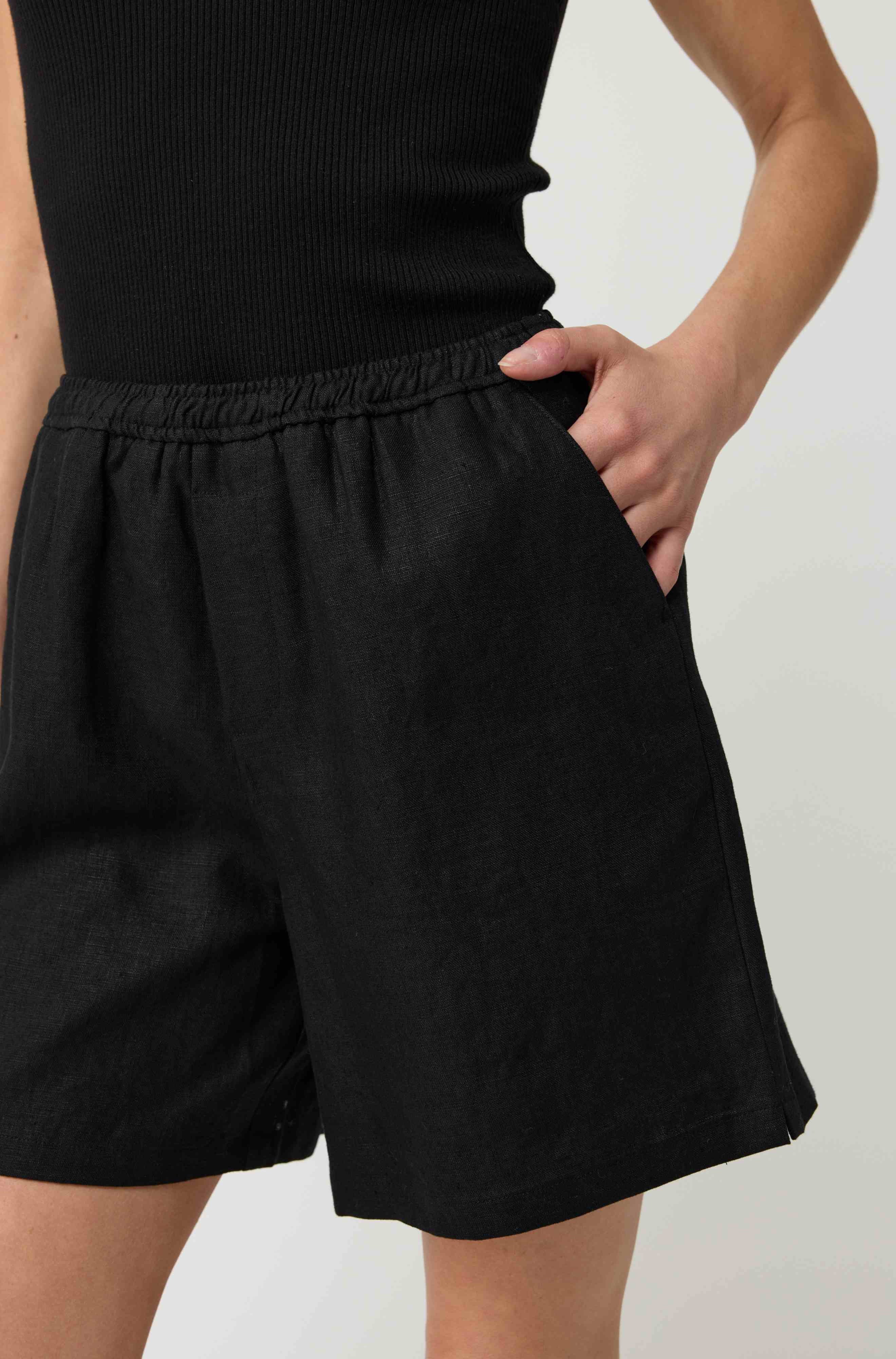 Woman wearing a black tank top and black linen shorts
